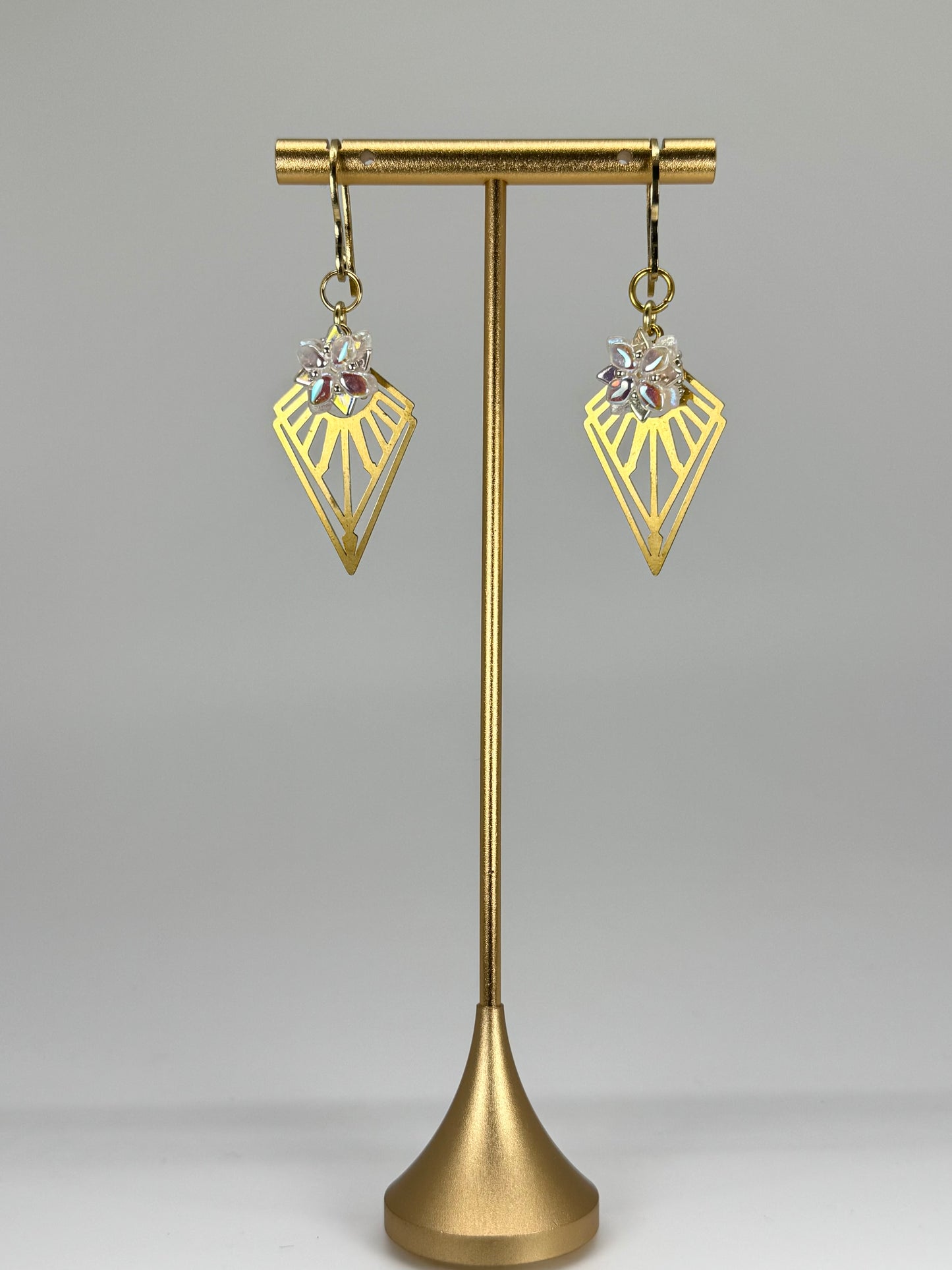 Gold earrings on a gold stand against a gray background