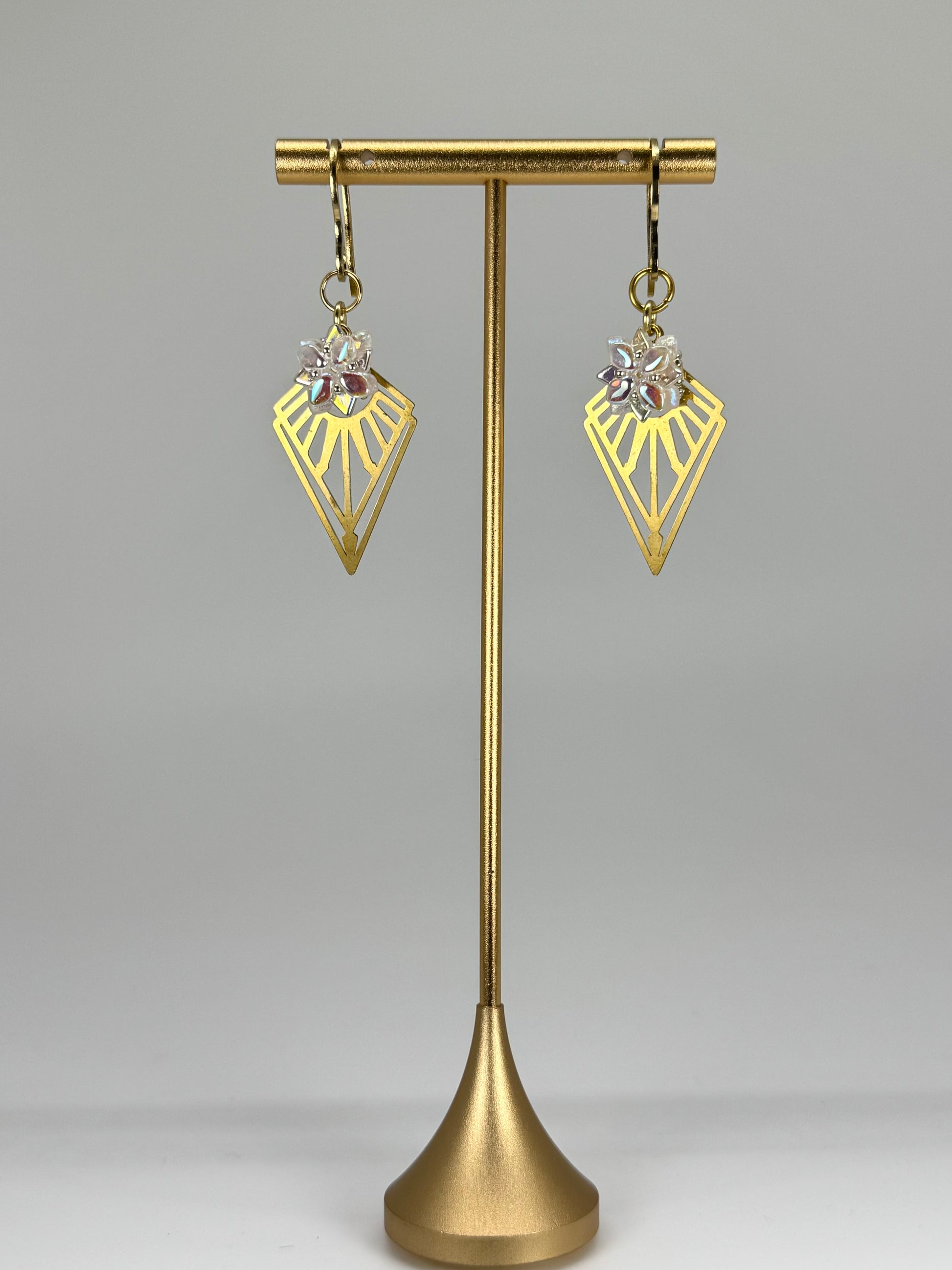 Gold earrings on a gold stand against a gray background