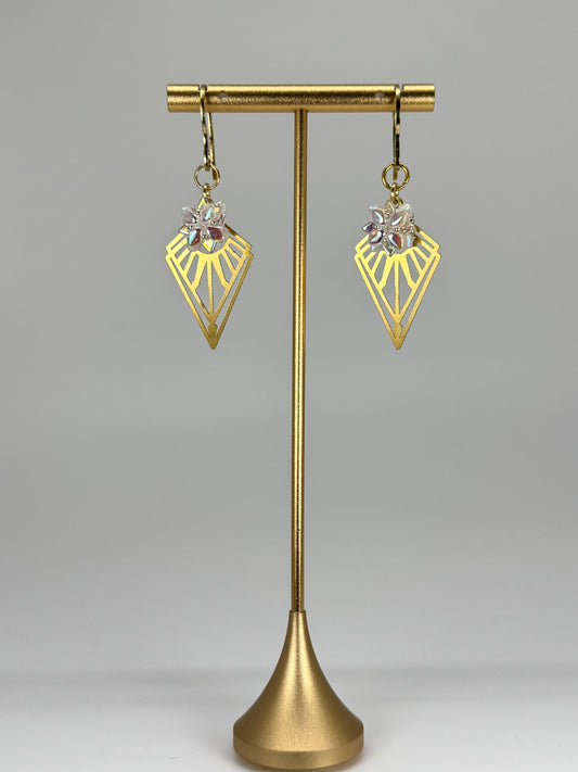 Gold earrings on a gold stand against a gray background