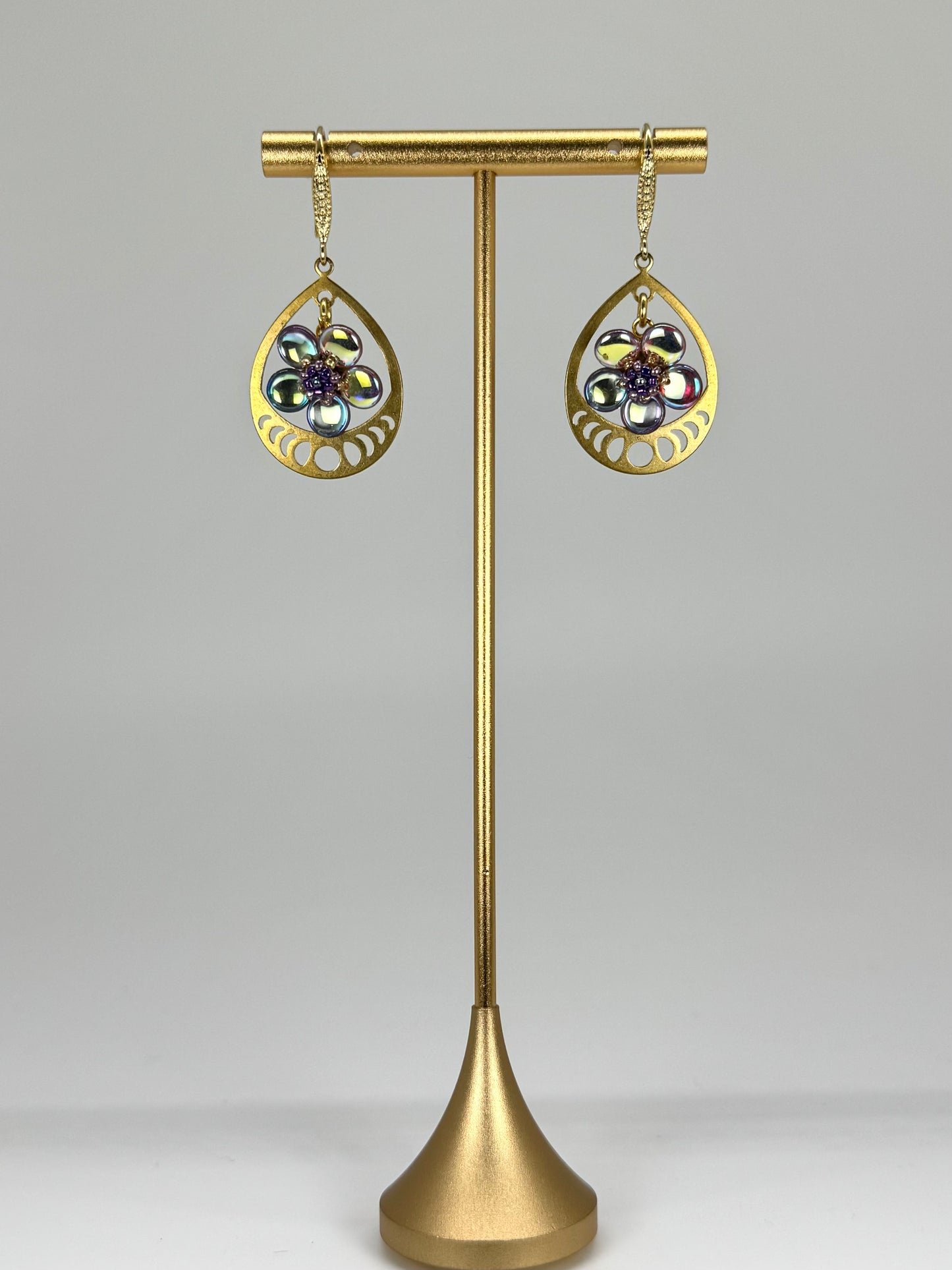 Gold earrings on a stand with a gray background