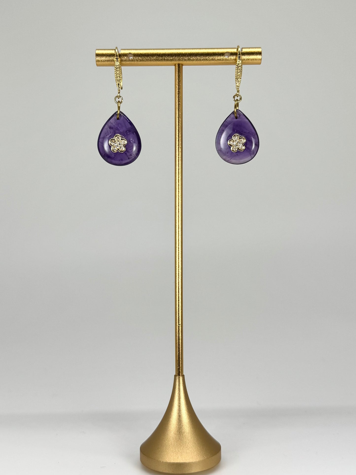 Purple teardrop earrings on a gold stand against a white background