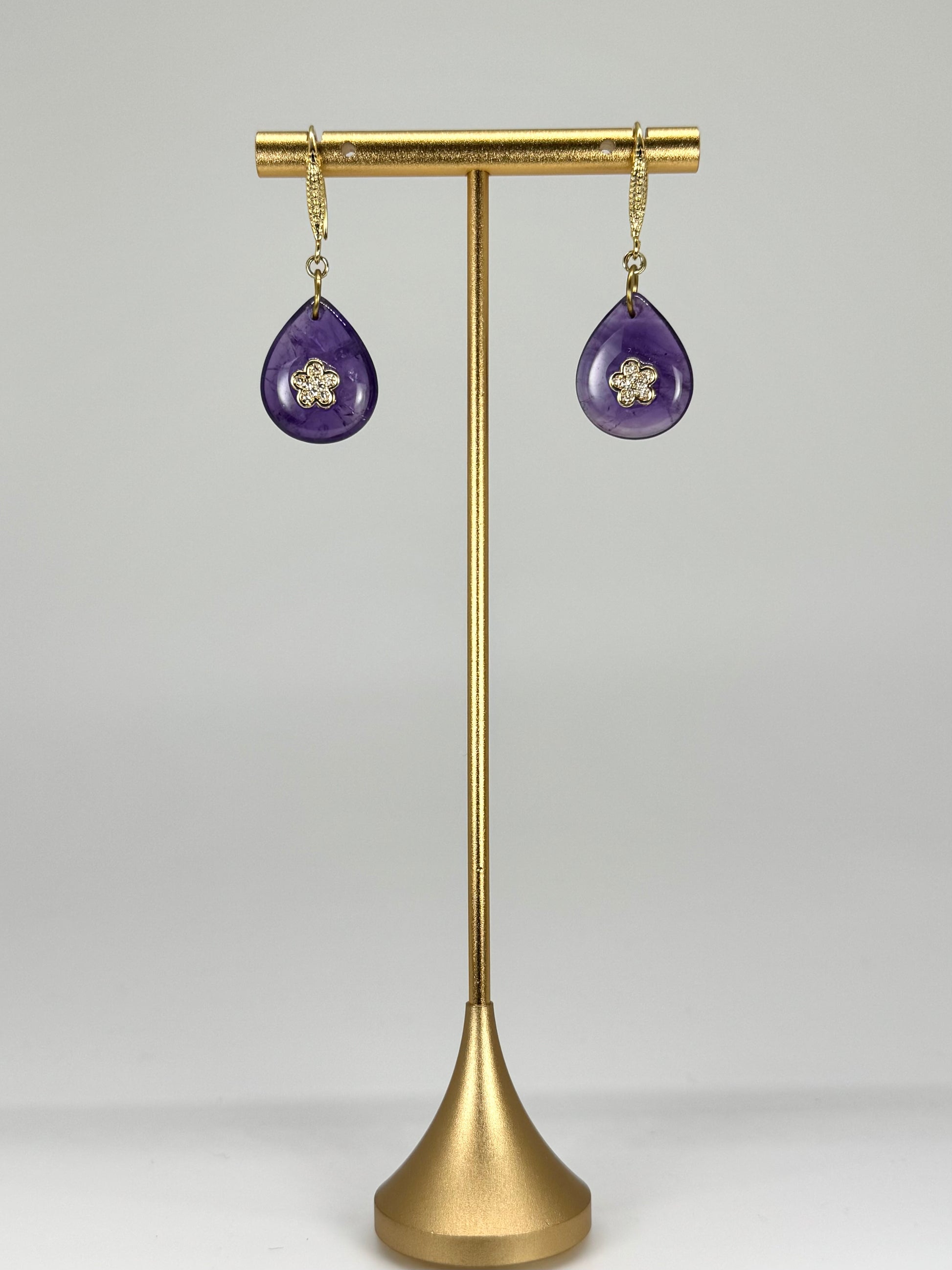 Purple teardrop earrings on a gold stand against a white background