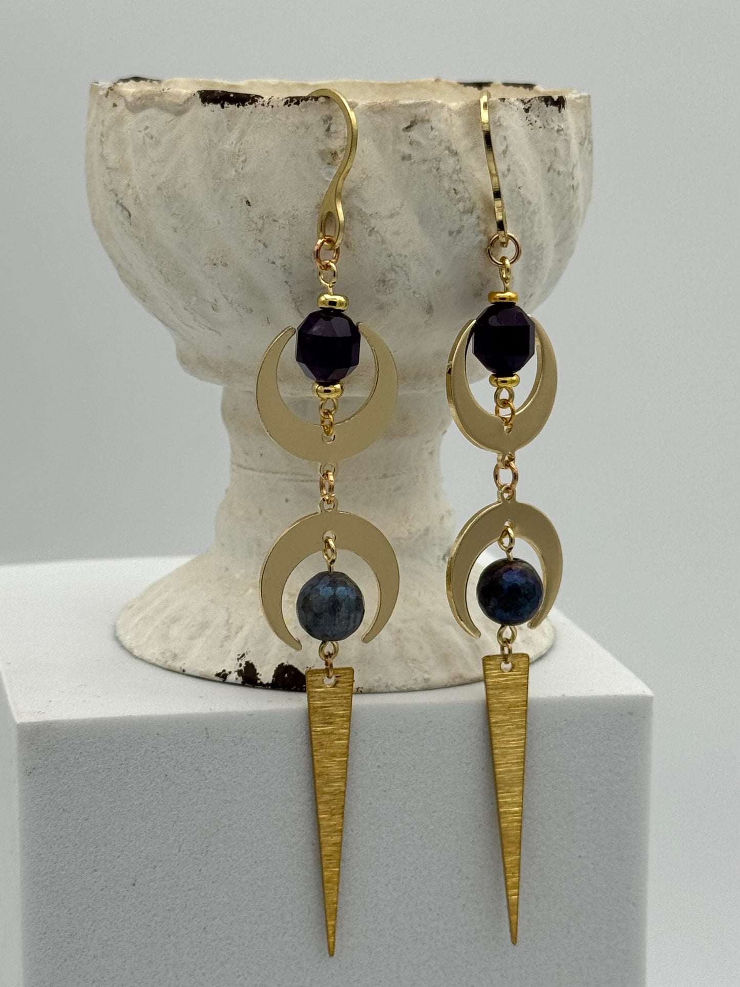 Gold earrings with black beads on a white pedestal