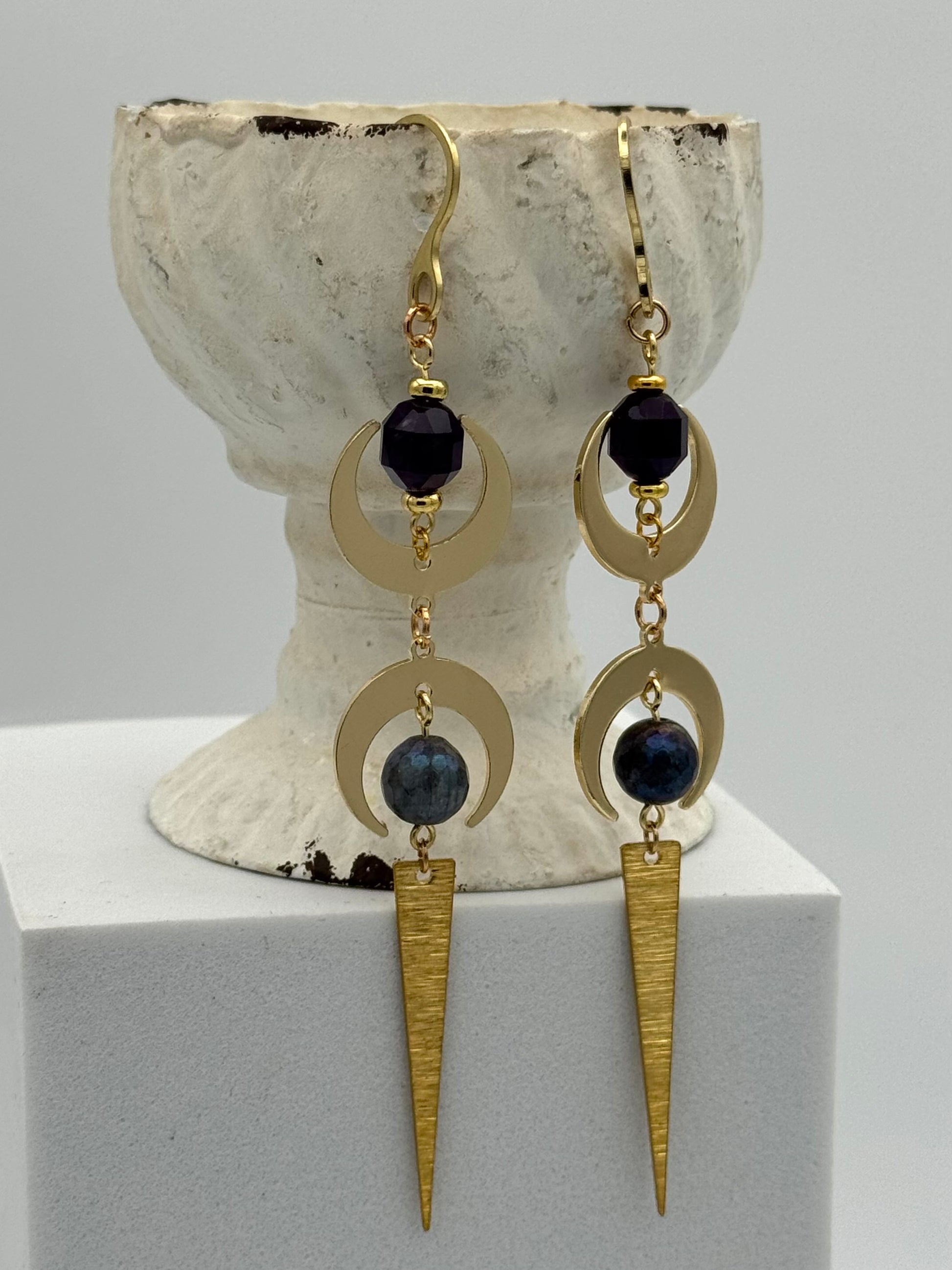 Gold earrings with black beads on a white pedestal