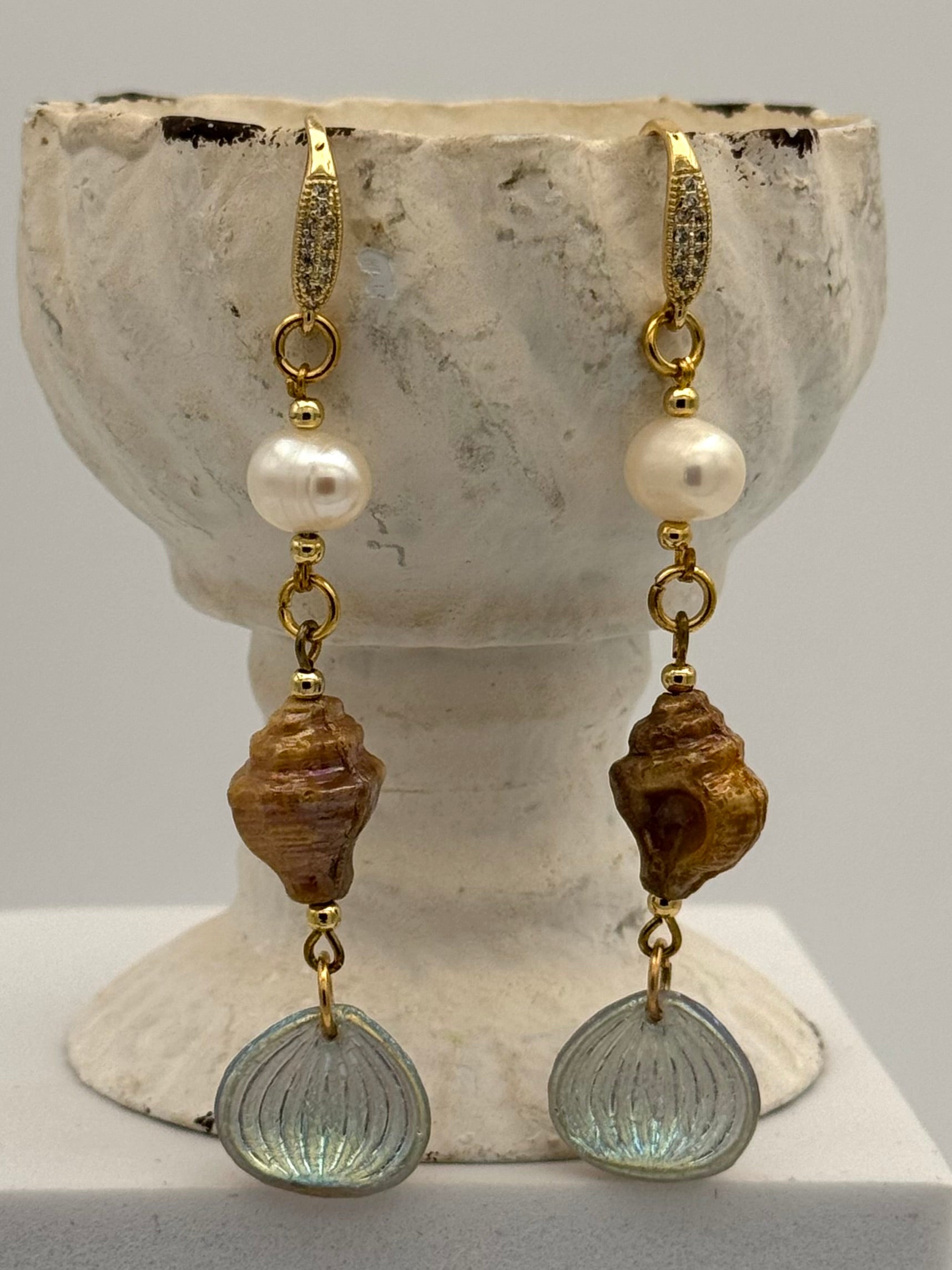 Pair of earrings with shell and pearl elements on a stone surface