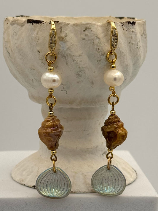 Pair of earrings with shell and pearl elements on a stone surface