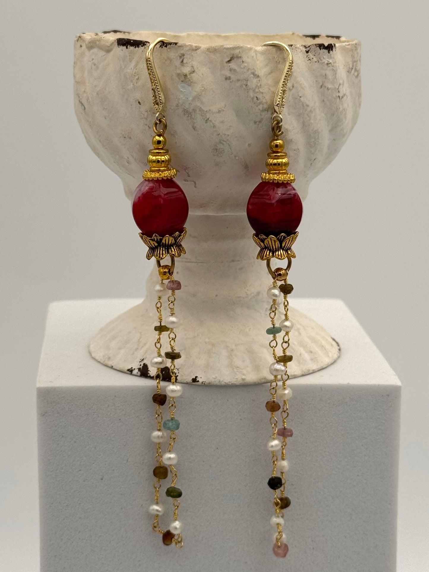Pair of earrings with red beads and long chains on a white stand.
