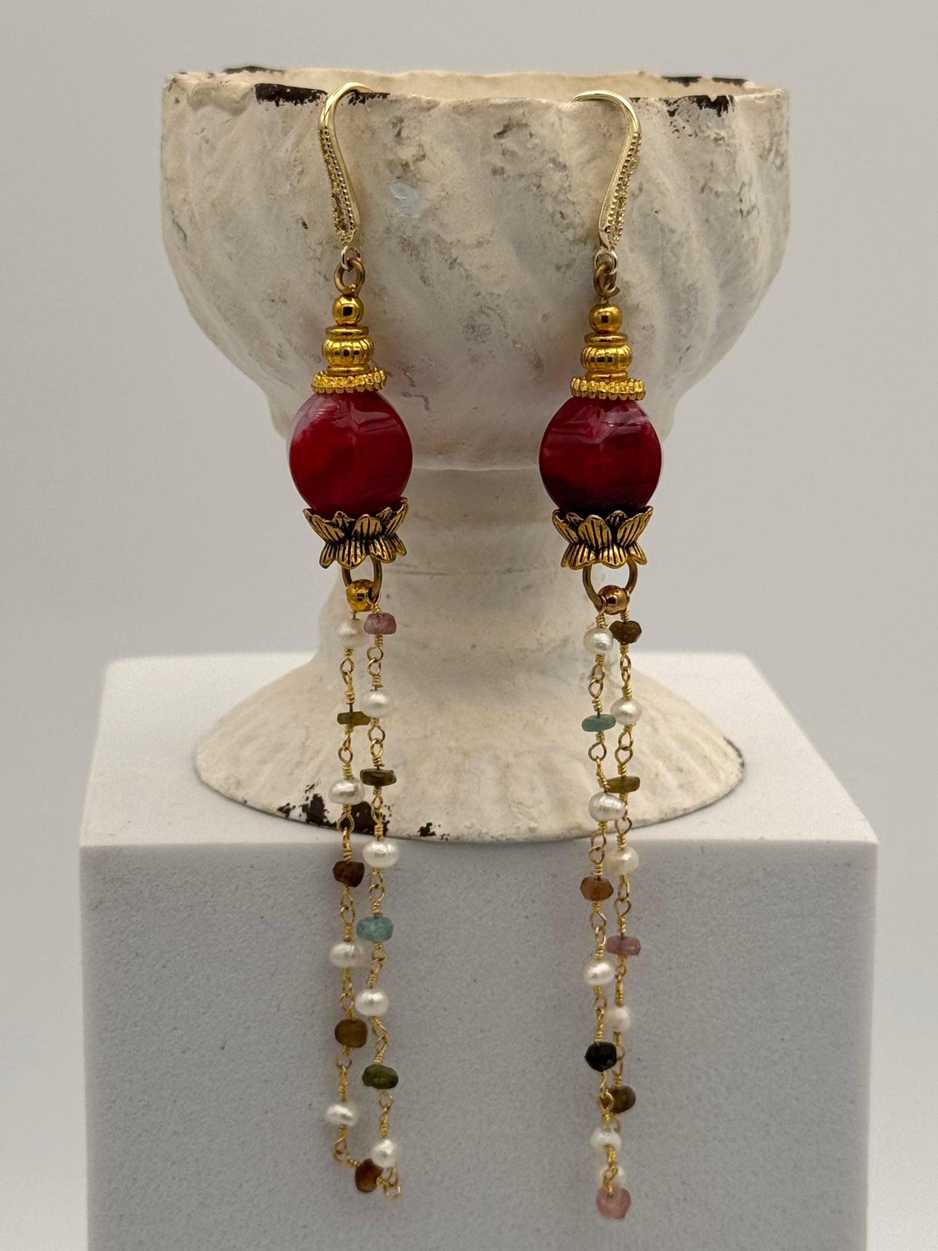 Pair of earrings with red beads and long chains on a white stand.
