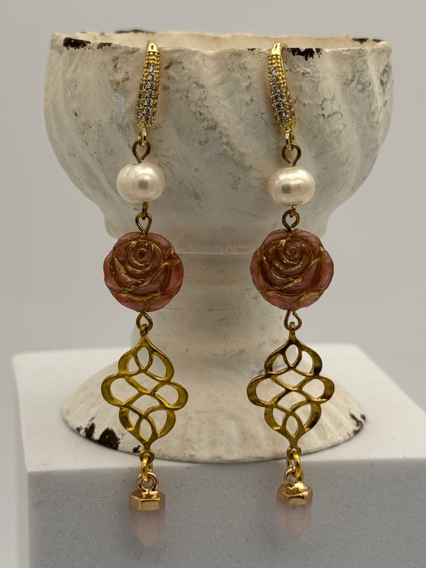 Pair of earrings with rose and pearl design on a stone surface