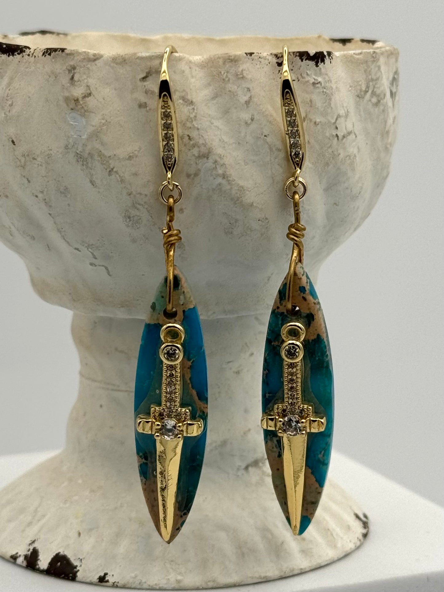 Pair of gold and turquoise earrings on a decorative stand.
