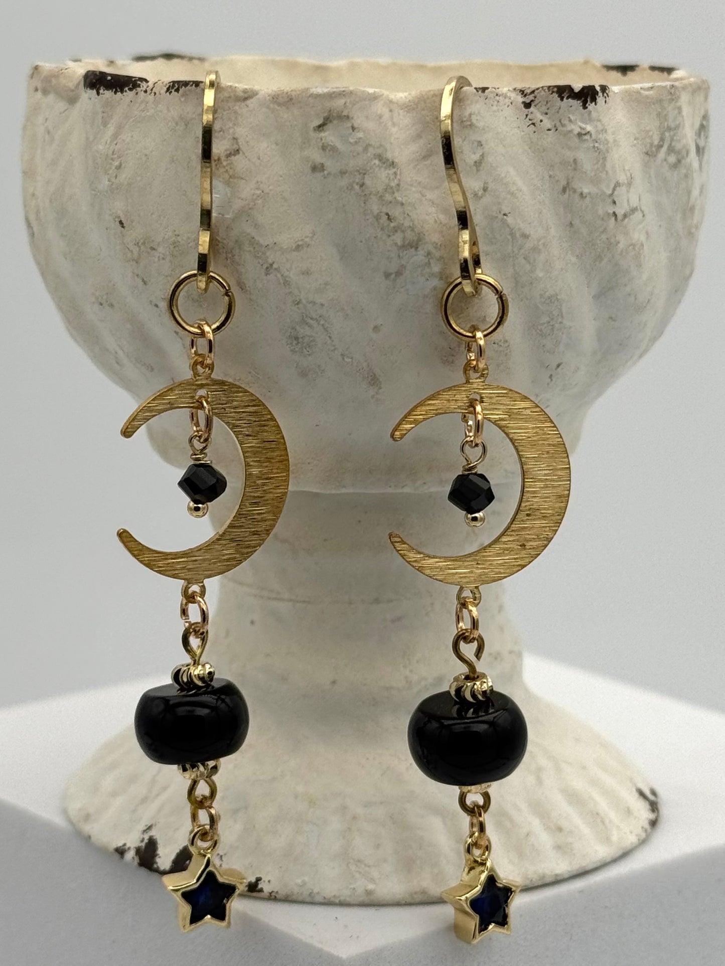 Gold crescent moon and star earrings with black beads on a stone surface