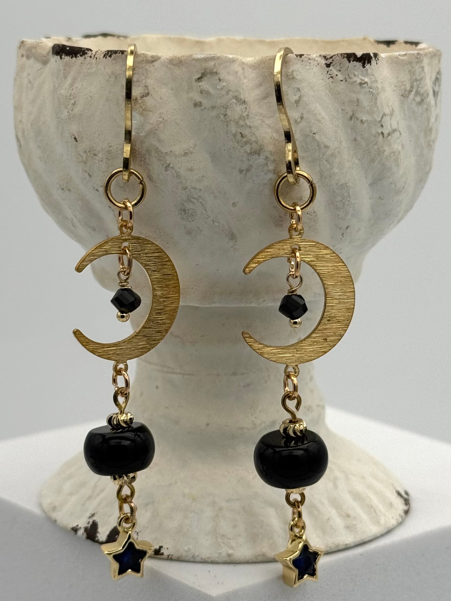 Gold crescent moon and star earrings with black beads on a stone surface