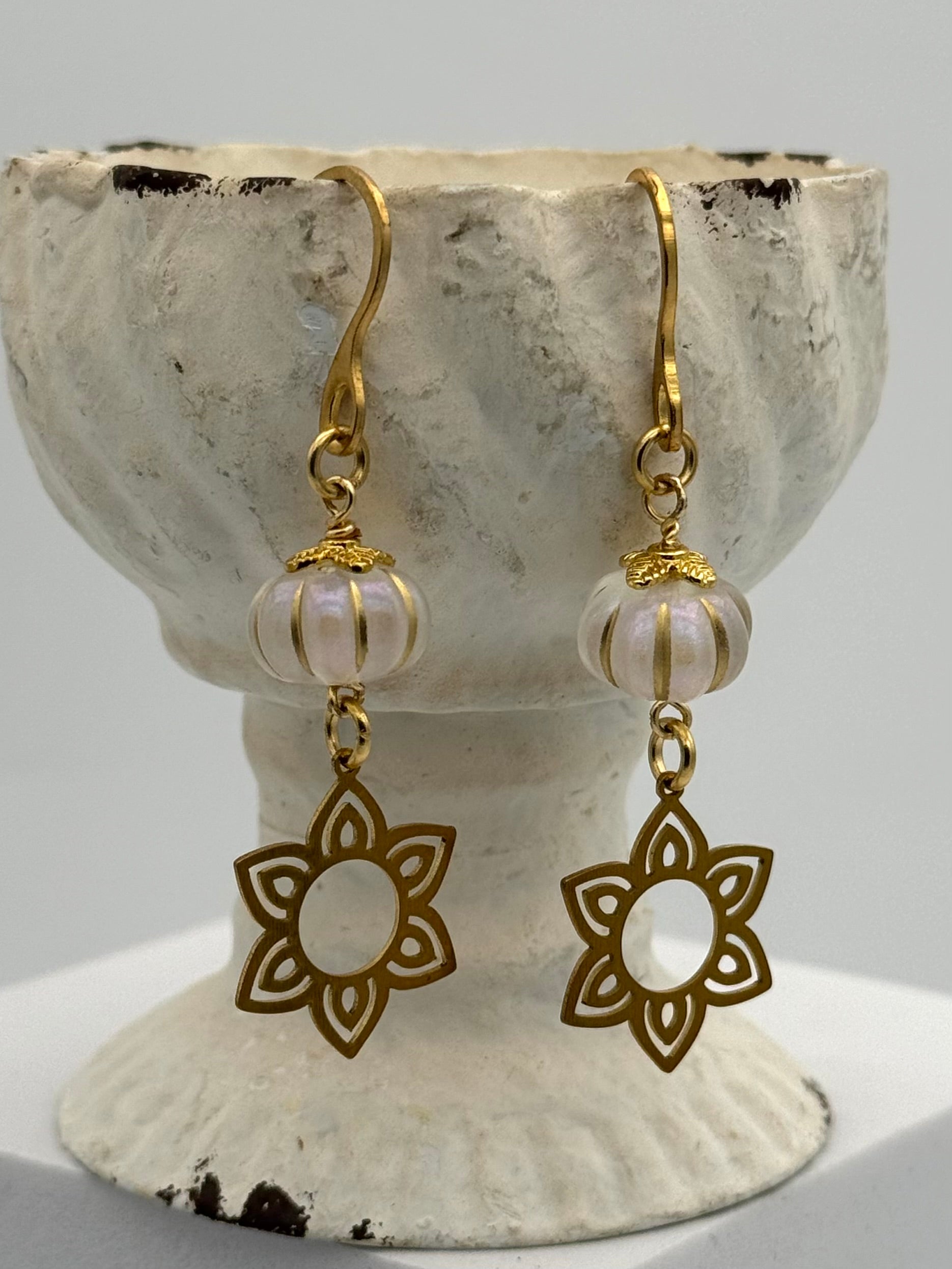 Gold earrings with floral designs and pearl-like beads on a textured stone stand.