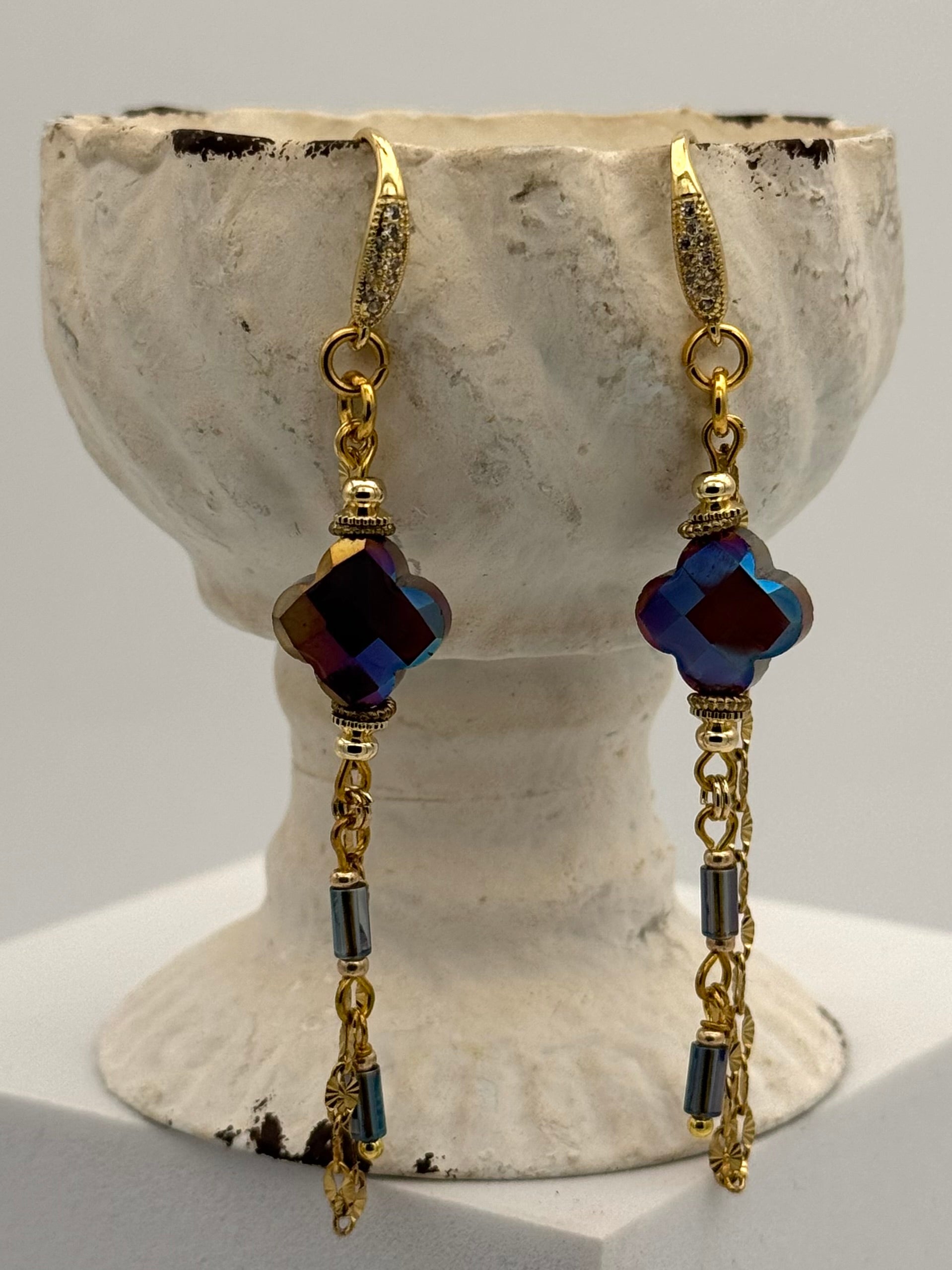 Pair of gold and blue beaded earrings on a textured stone stand.