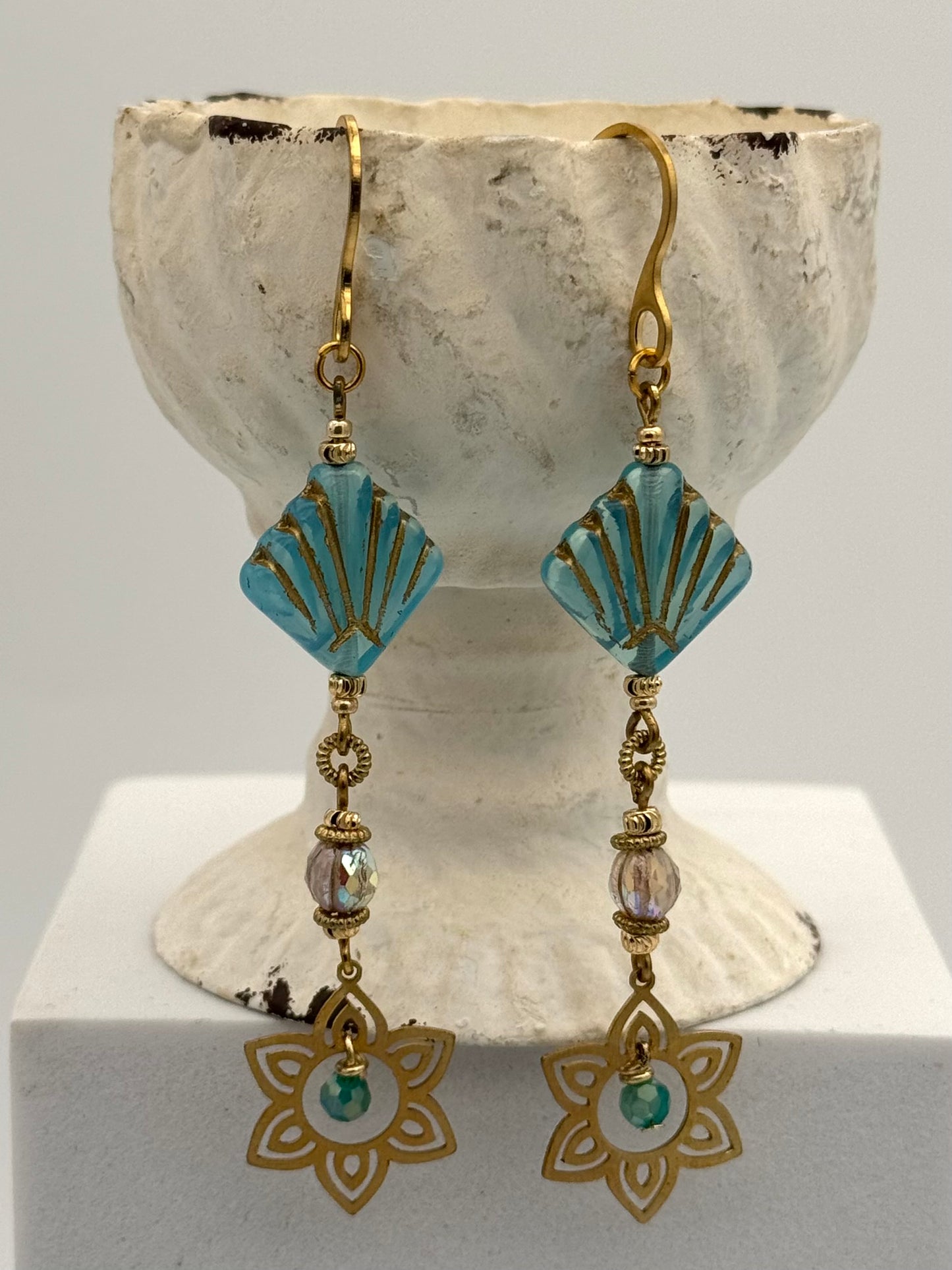 Pair of earrings with turquoise and gold design on a white stand.