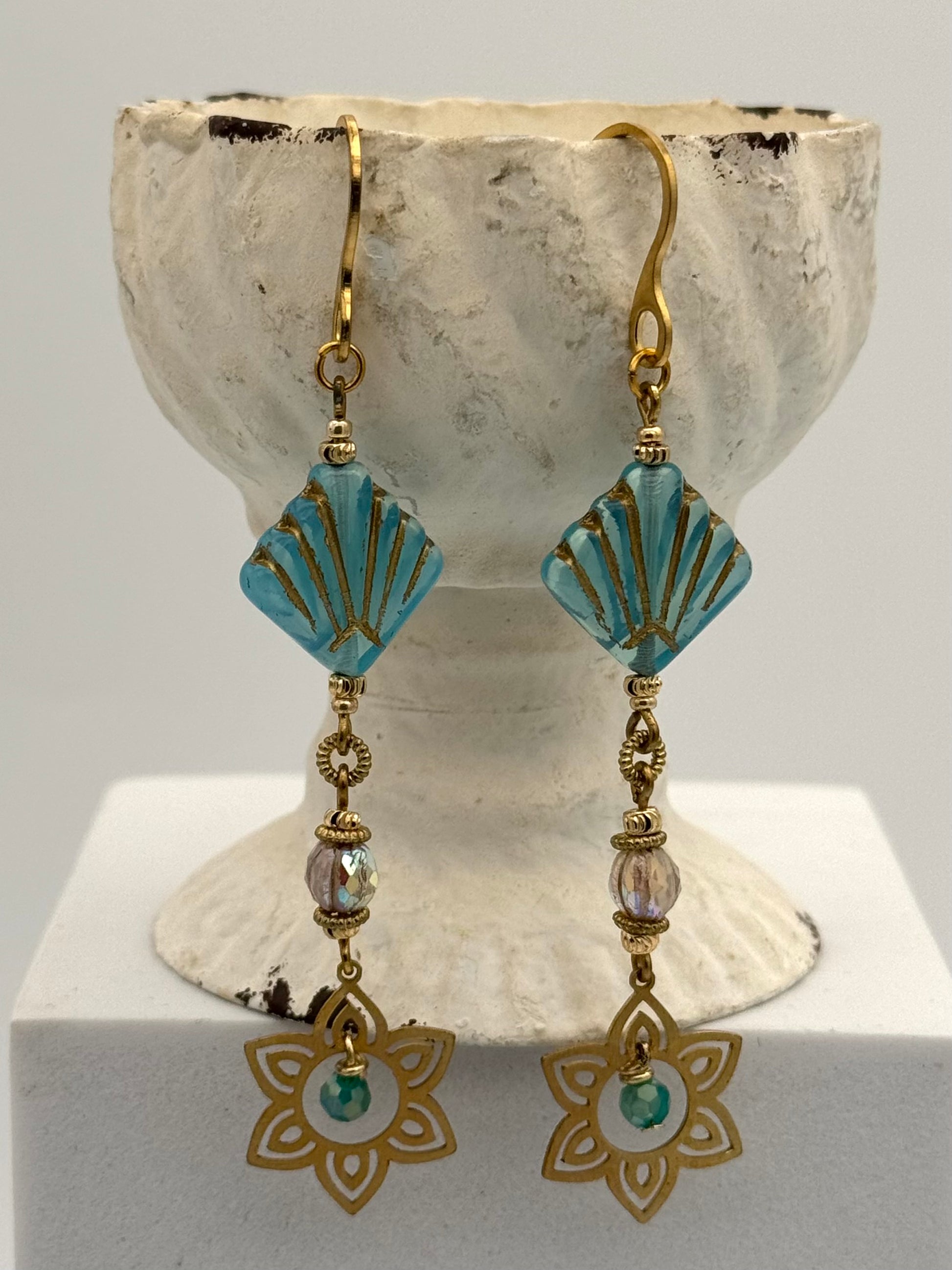 Pair of earrings with turquoise and gold design on a white stand.