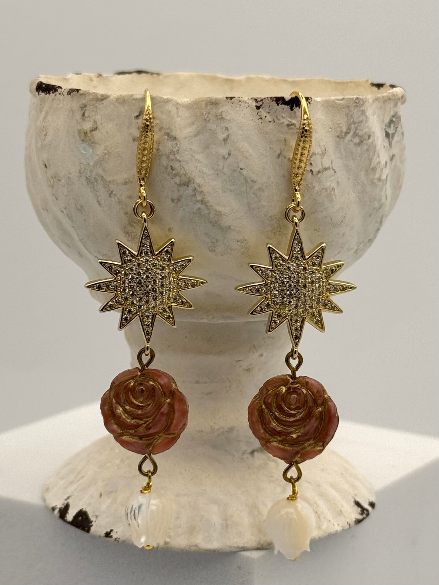 Gold star and rose earrings on a shell with a gray background