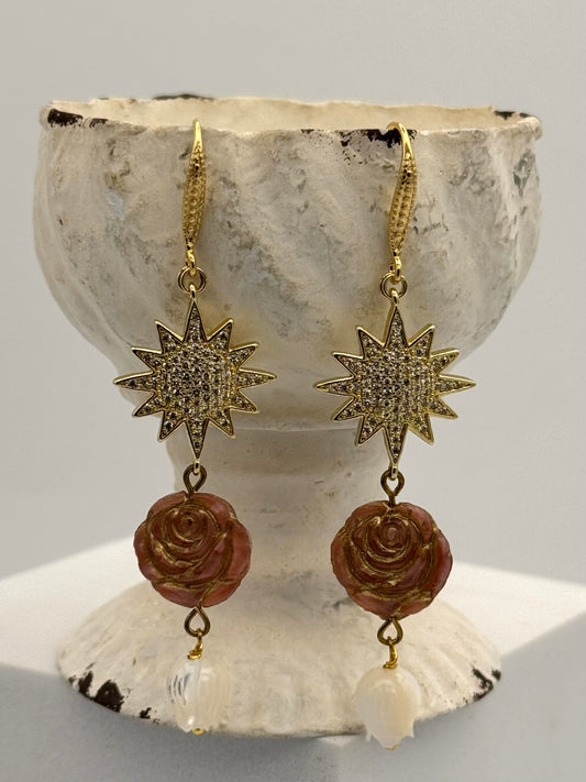 Gold star and rose earrings on a shell with a gray background
