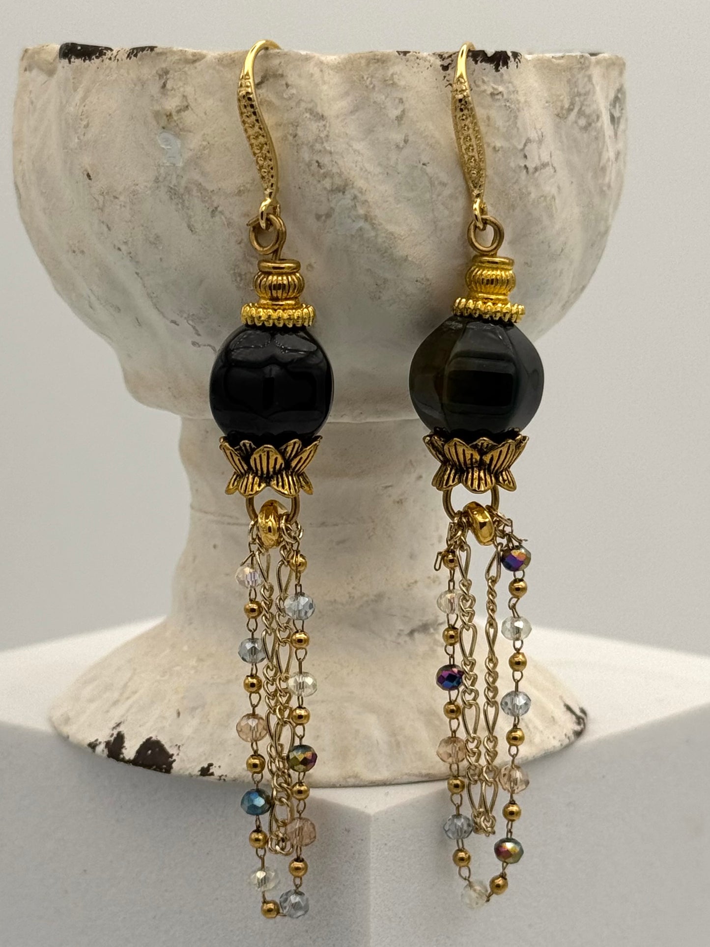 Pair of earrings with black beads and gold accents on a decorative stand.