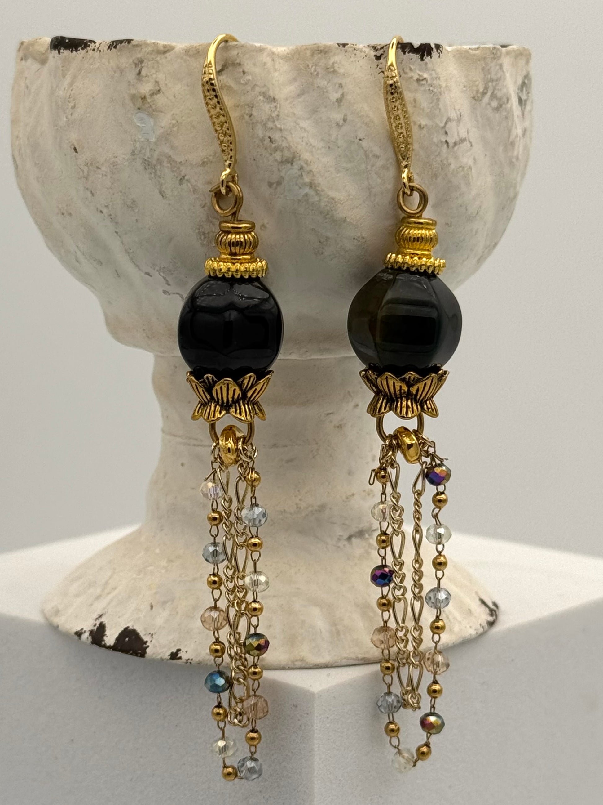 Pair of earrings with black beads and gold accents on a decorative stand.