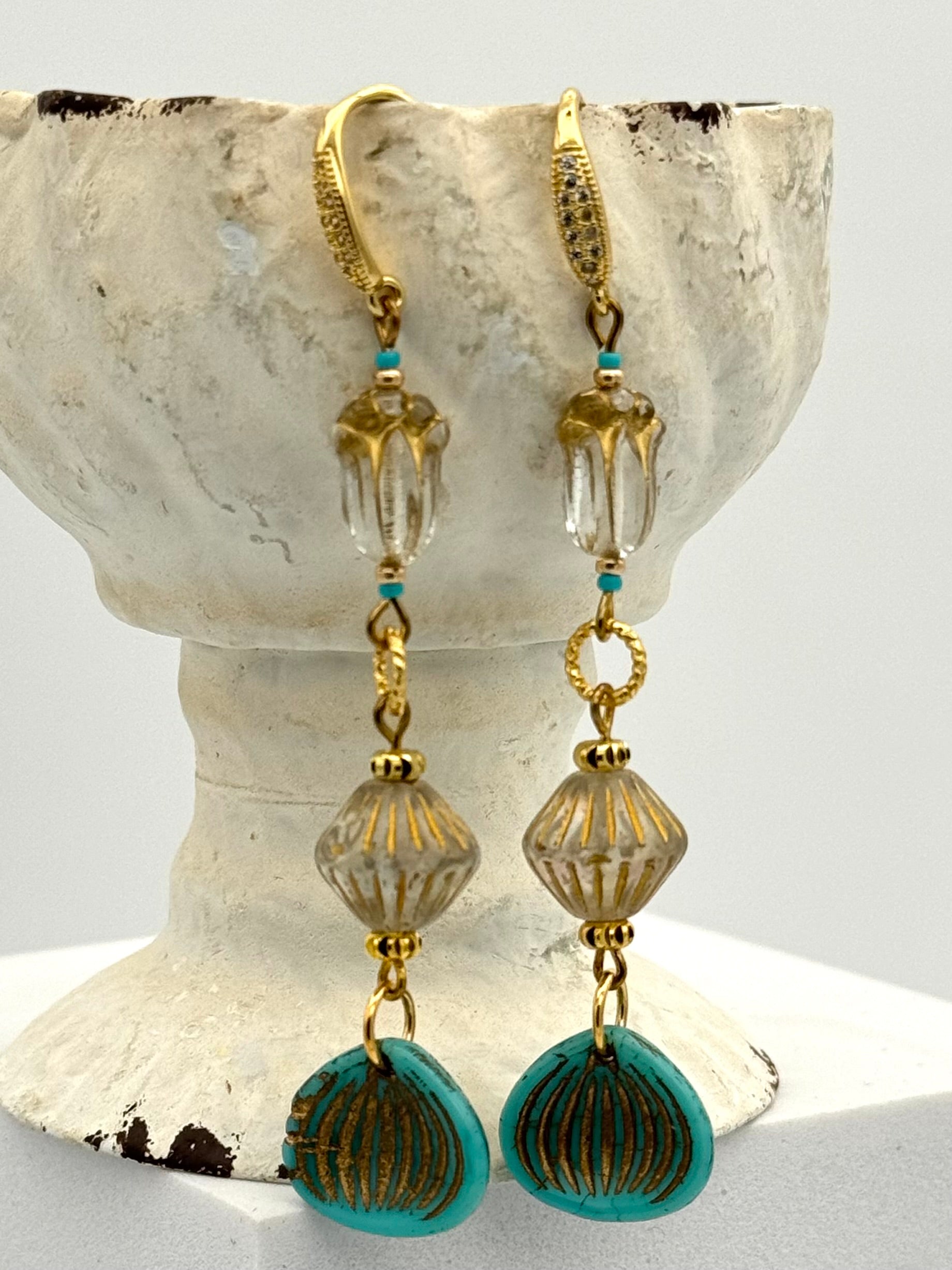 Gold and turquoise beaded earrings on a shell-shaped stand.