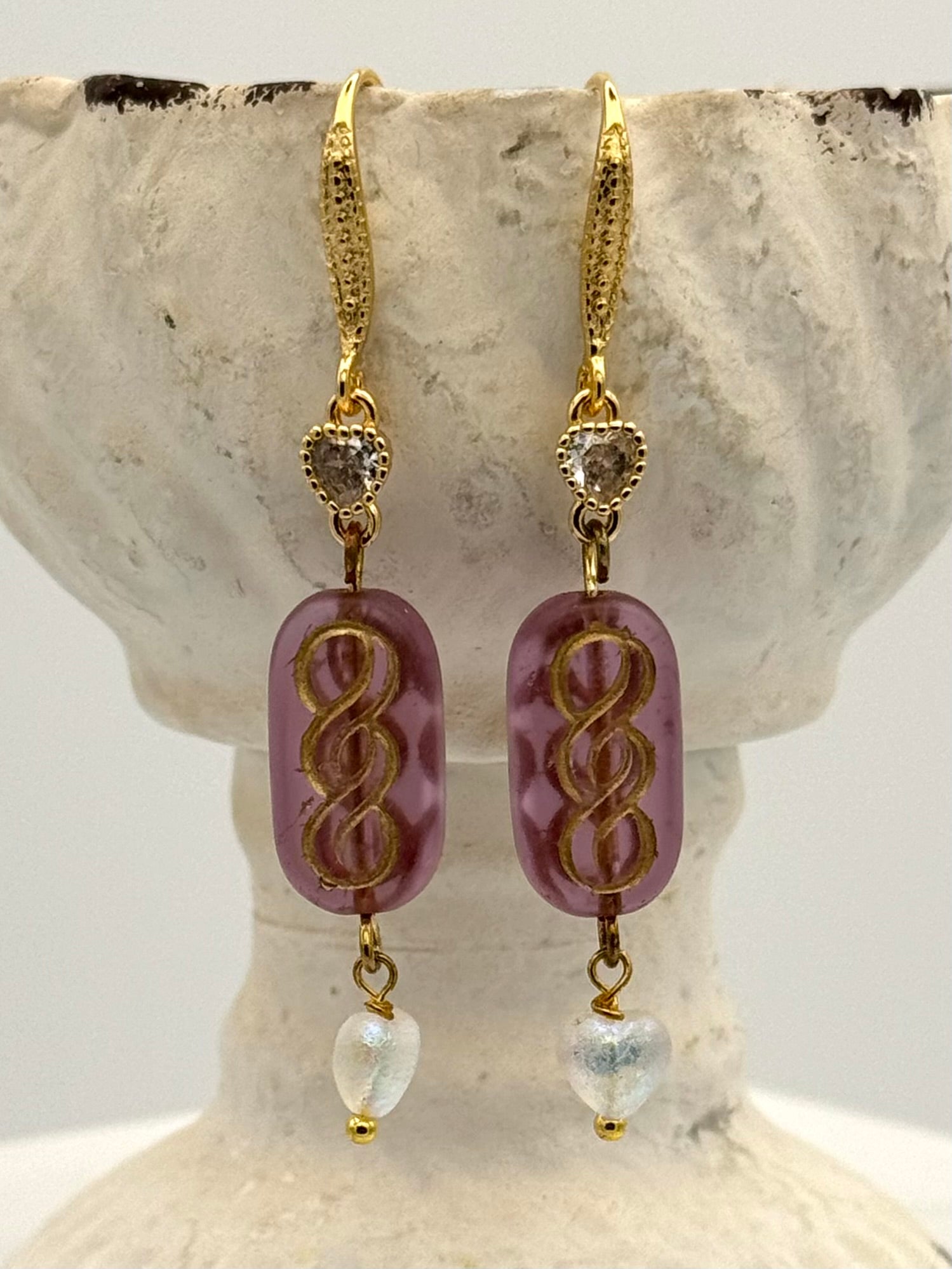 Gold and purple earrings on a decorative stone surface