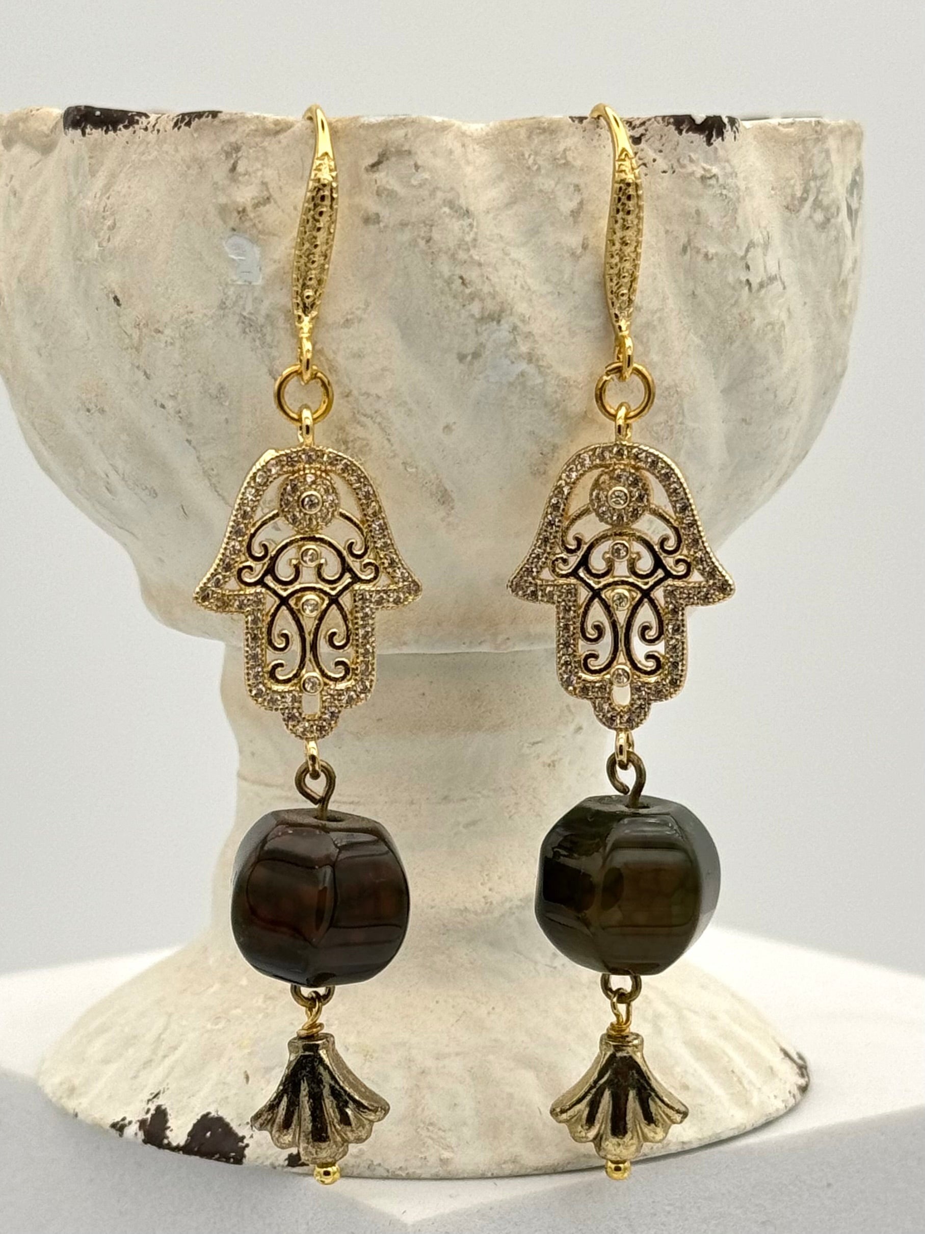 Pair of gold and black Hamsa hand earrings on a stone surface