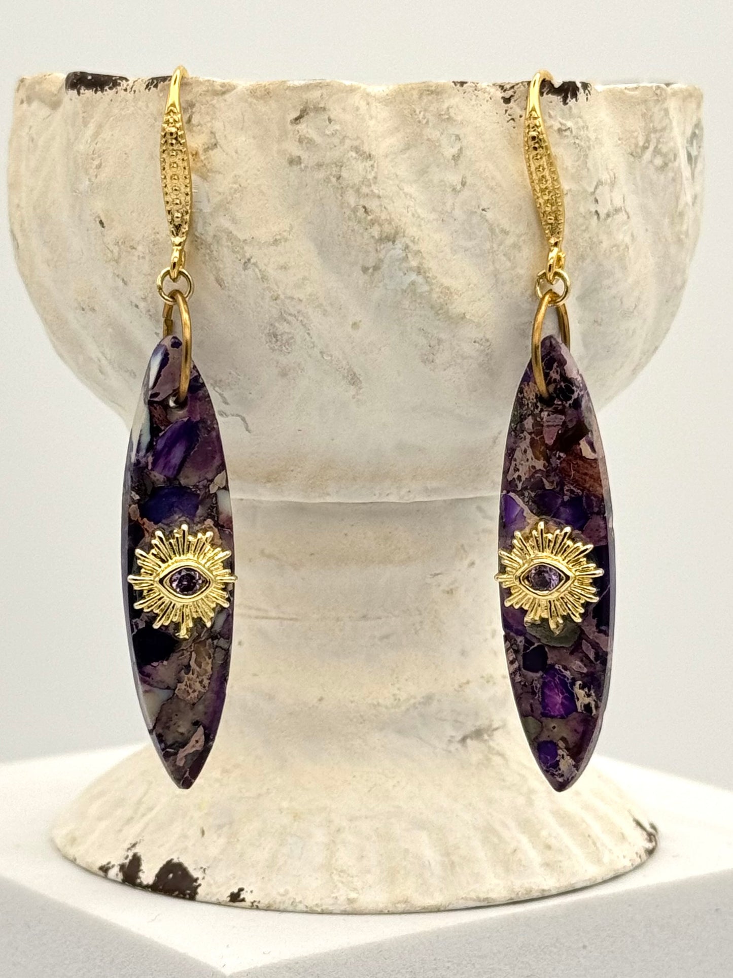 Pair of purple earrings with gold accents on a white stone stand.
