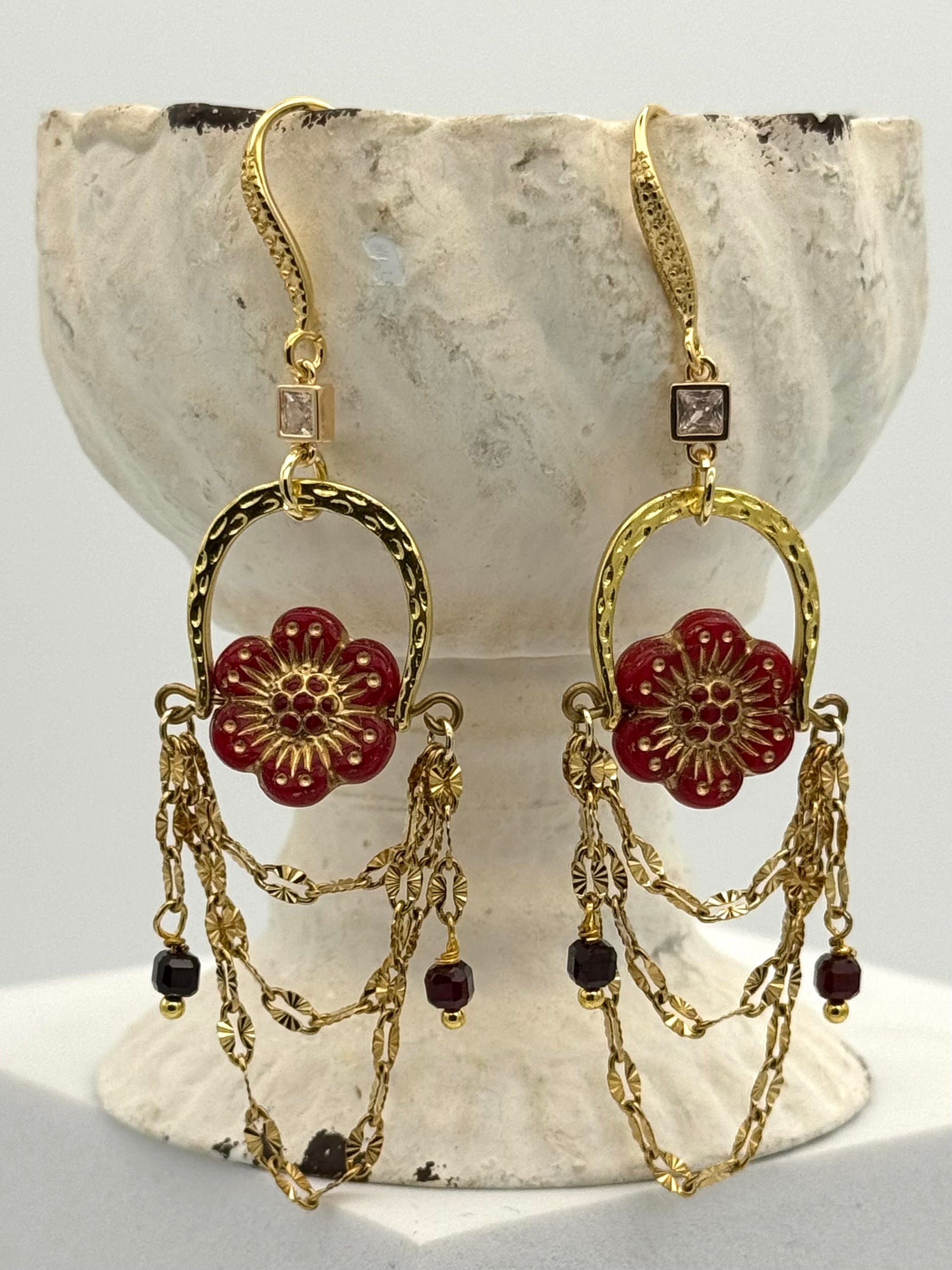 Gold and red floral earrings on a stone surface
