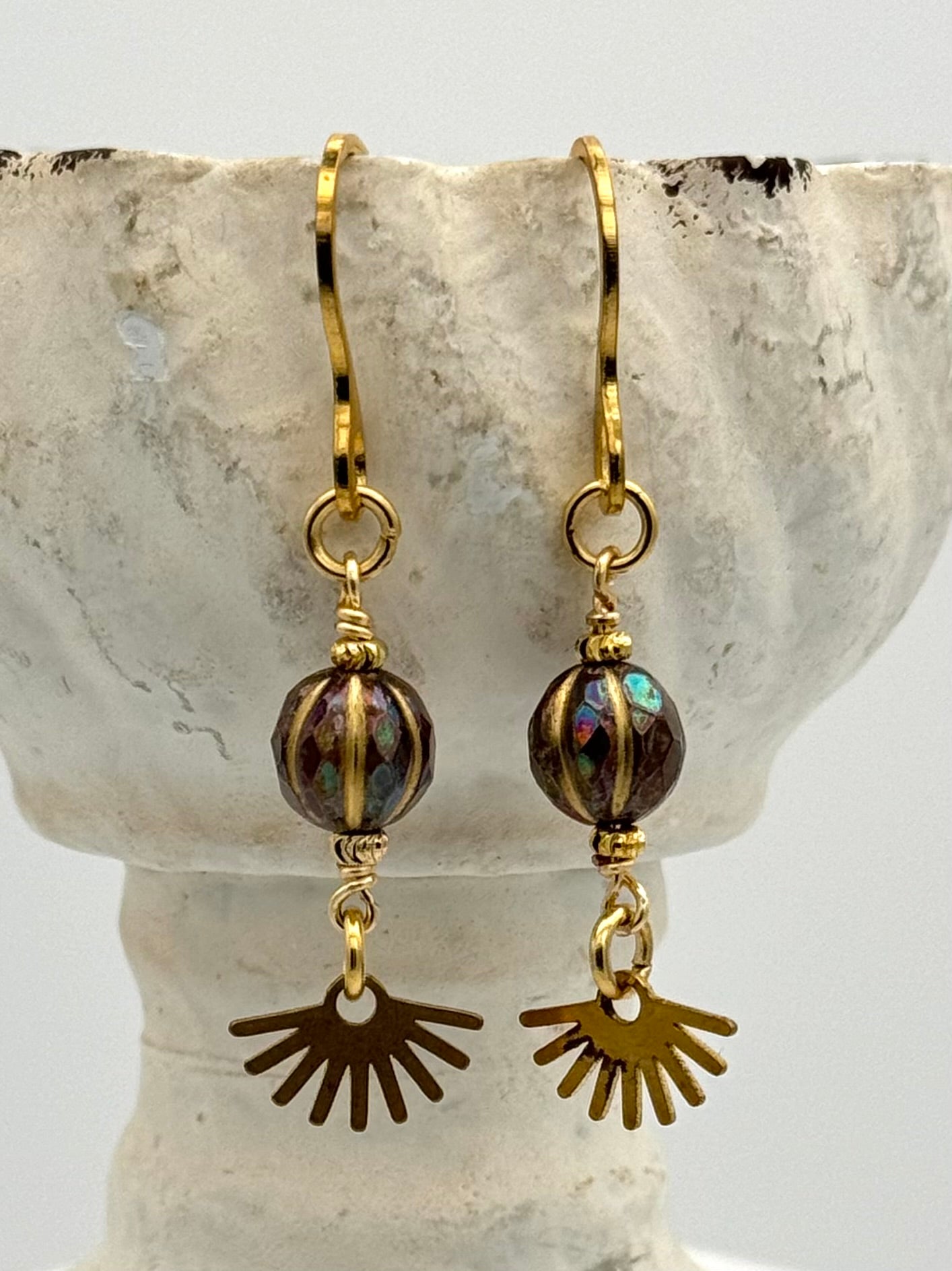 Gold earrings with sun-shaped charms on a stone surface