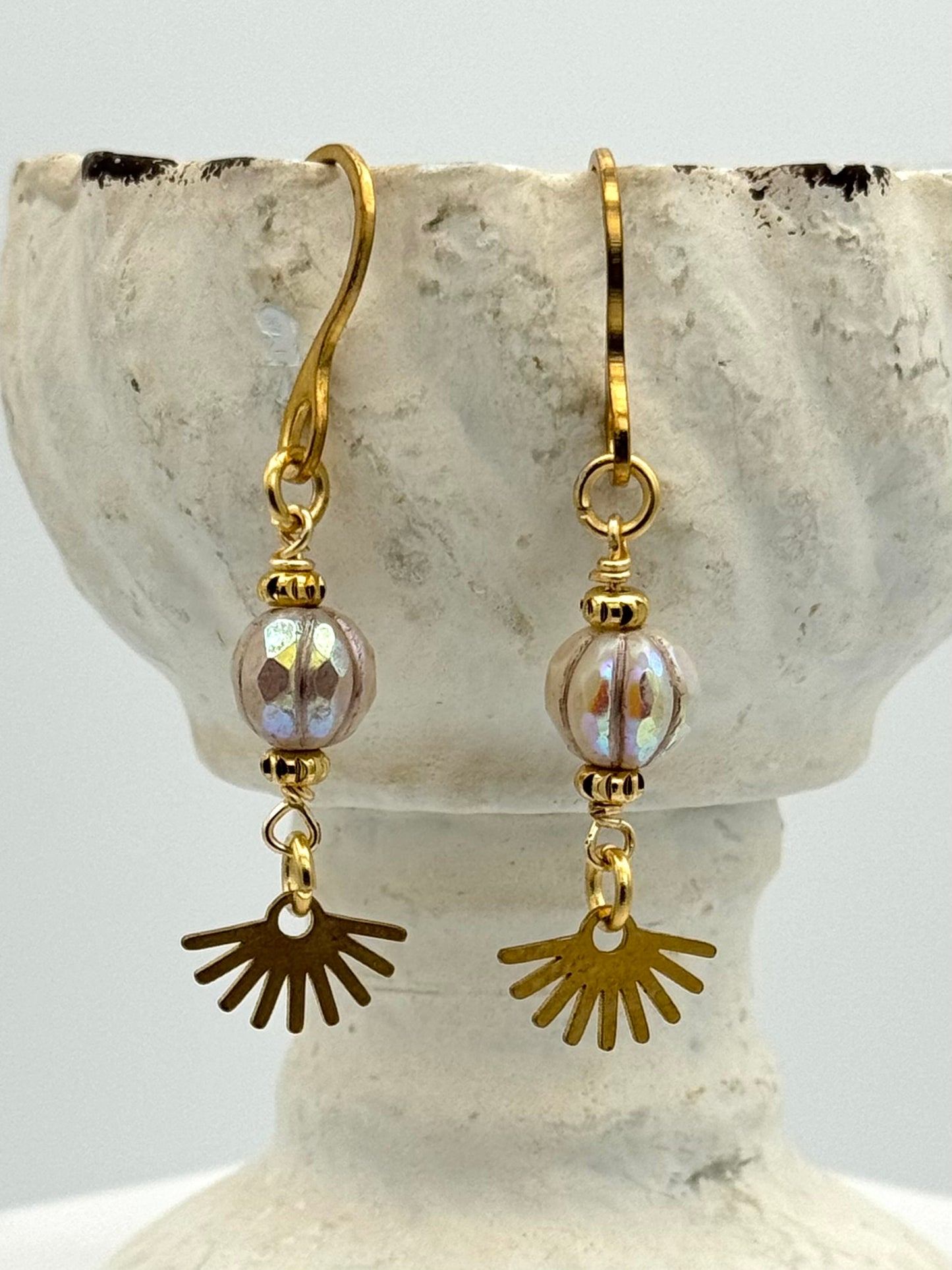 Gold and brass earrings with sunburst charms on a stone surface