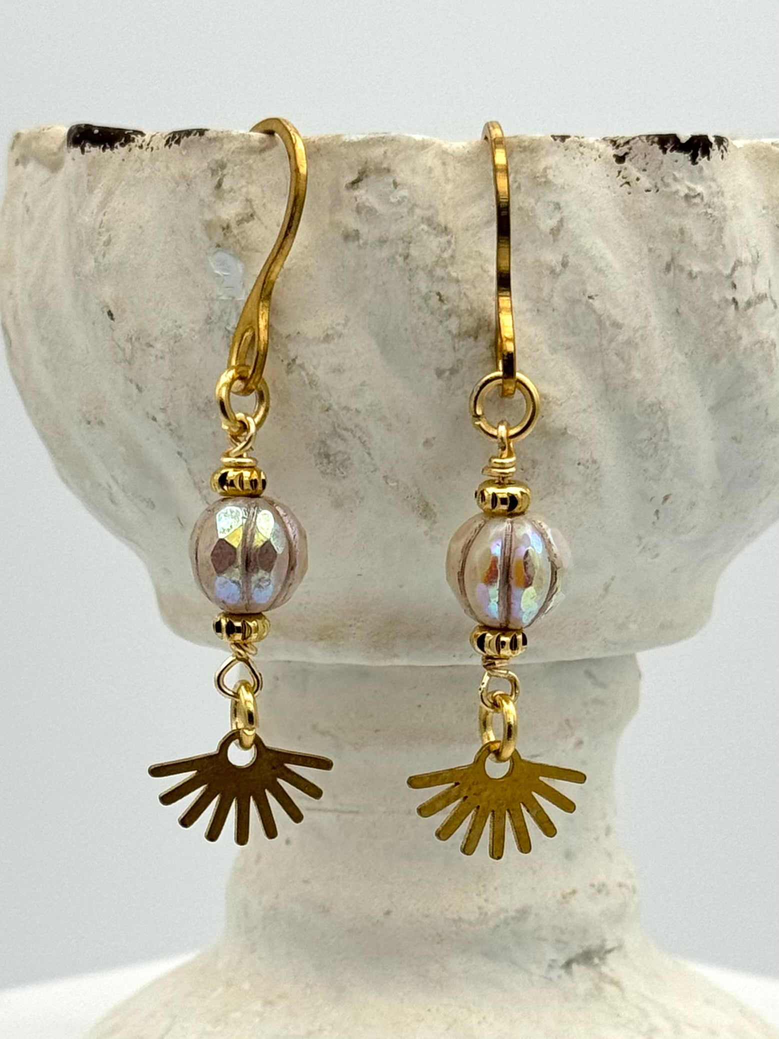 Gold and brass earrings with sunburst charms on a stone surface