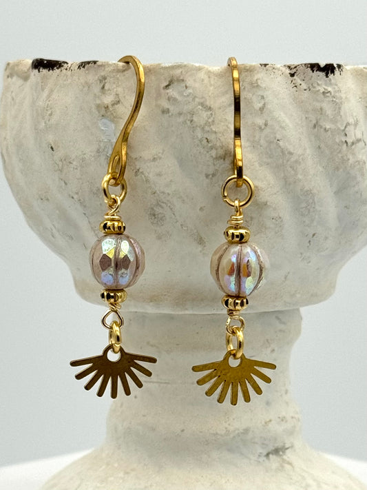 Gold and brass earrings with sunburst charms on a stone surface