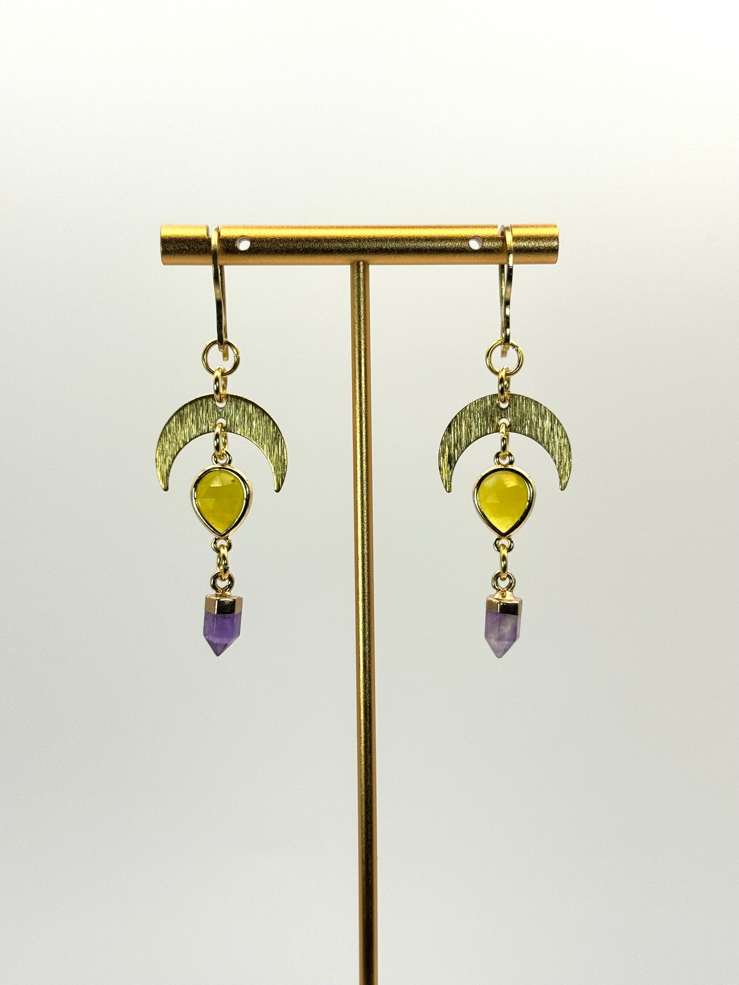 Gold earrings with yellow and purple gemstones on a white background