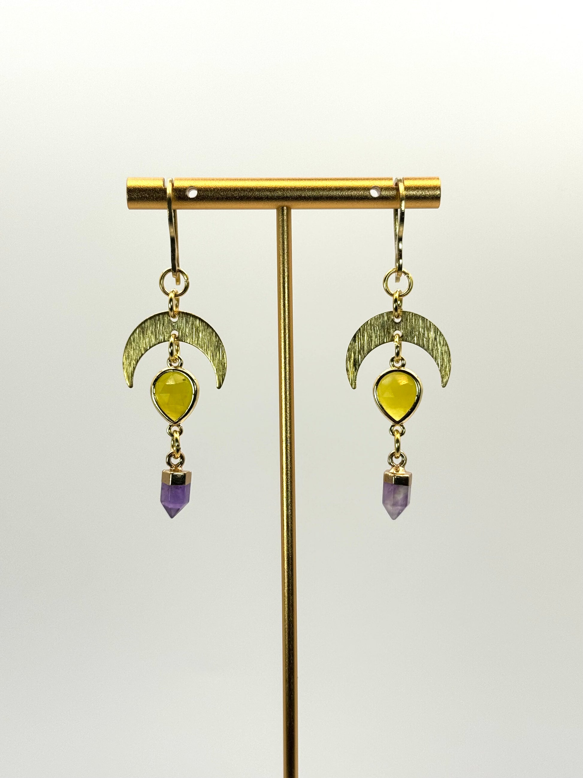 Gold earrings with yellow and purple gemstones on a white background