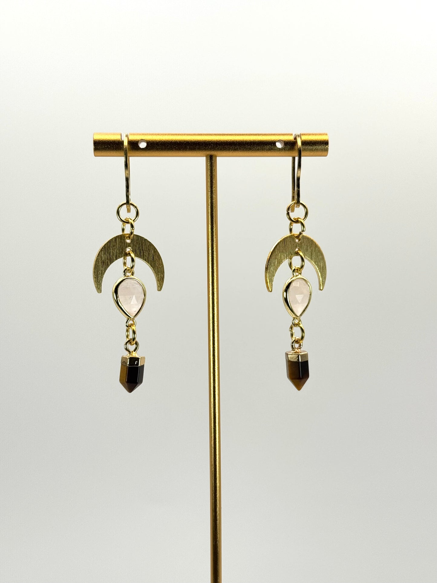 Gold earrings with moon-shaped hooks and gemstone drops on a white background