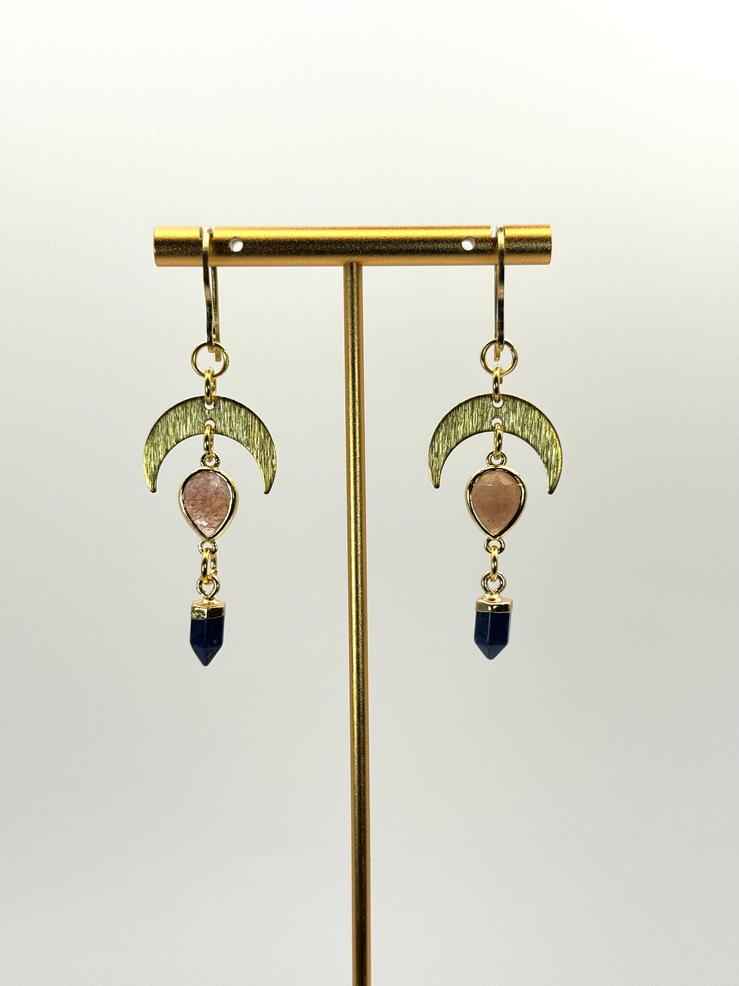 Pair of gold earrings with moon designs and gemstone drops on a white background