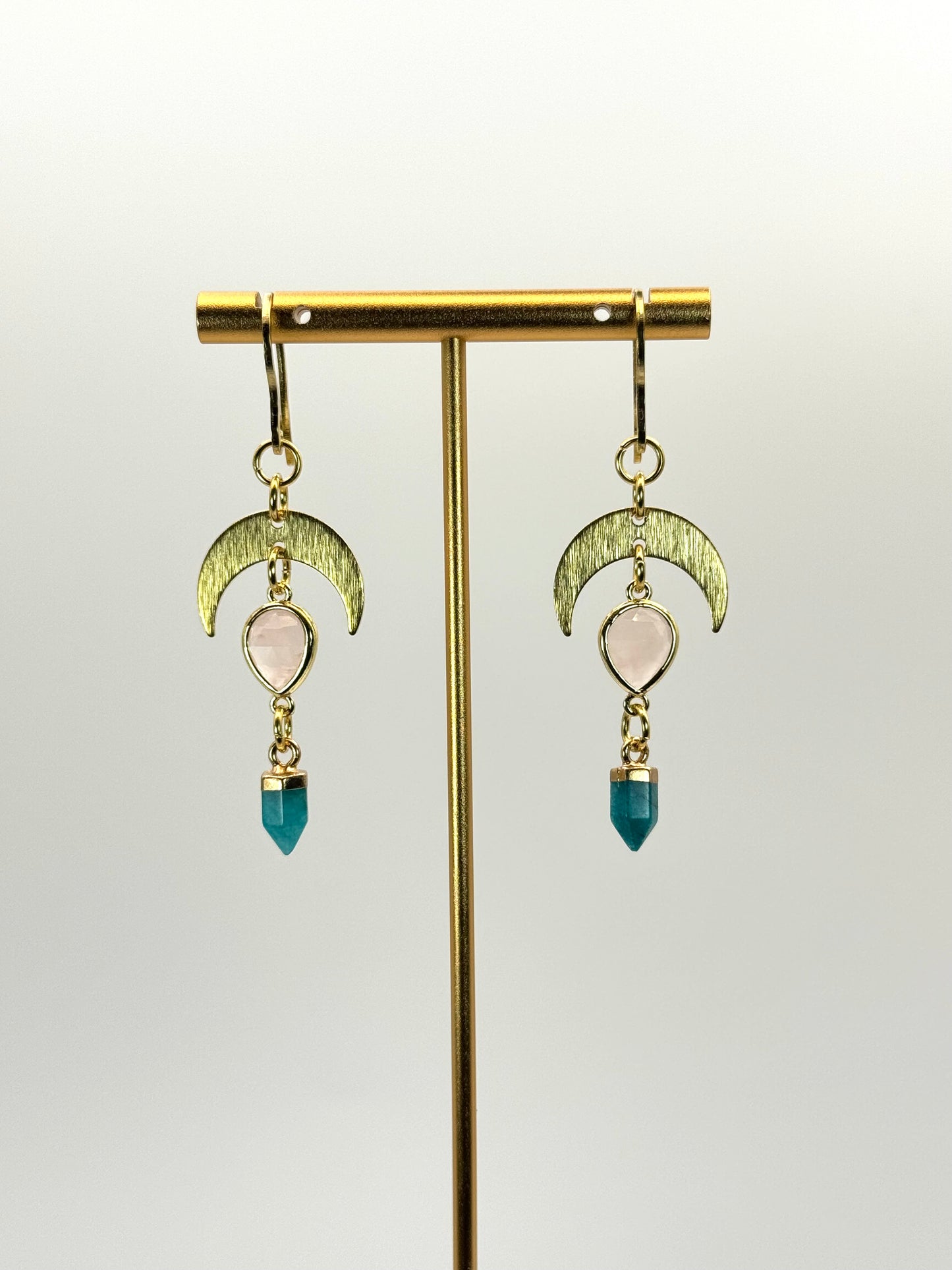 Gold earrings with moon-shaped designs and blue beads on a stand against a light background
