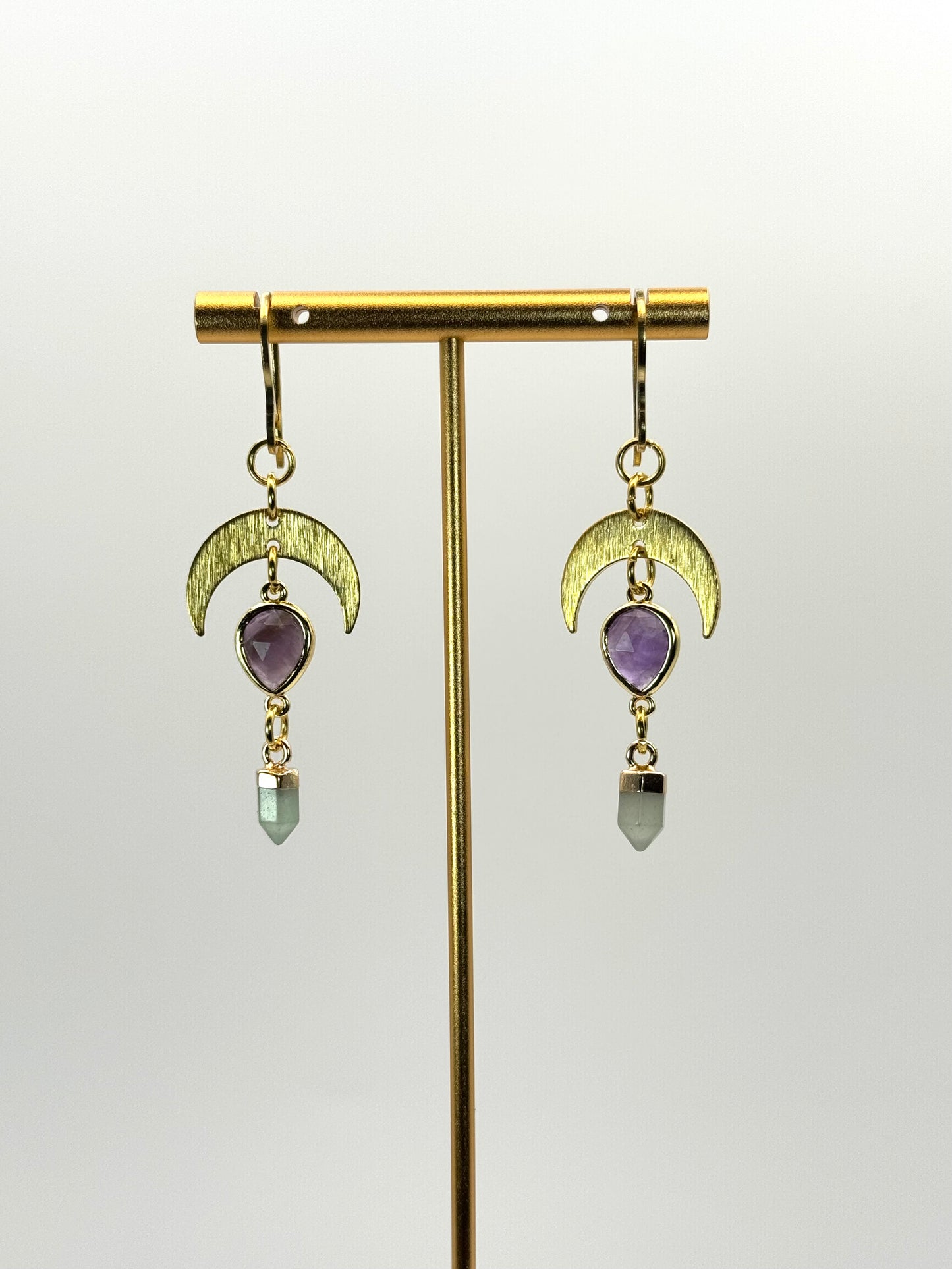 Gold earrings with purple gemstones on a white background