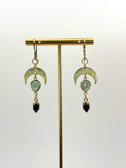 Pair of earrings with green gemstones and black beads on a gold stand against a white background