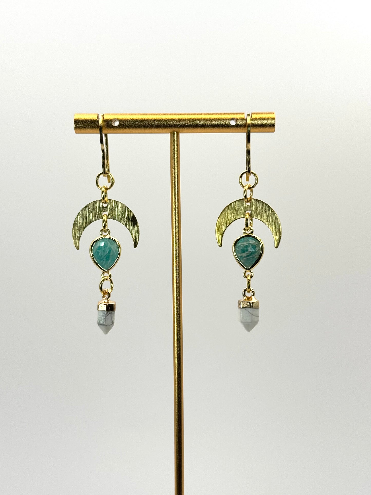 Pair of earrings with green gemstones and gold accents on a white background