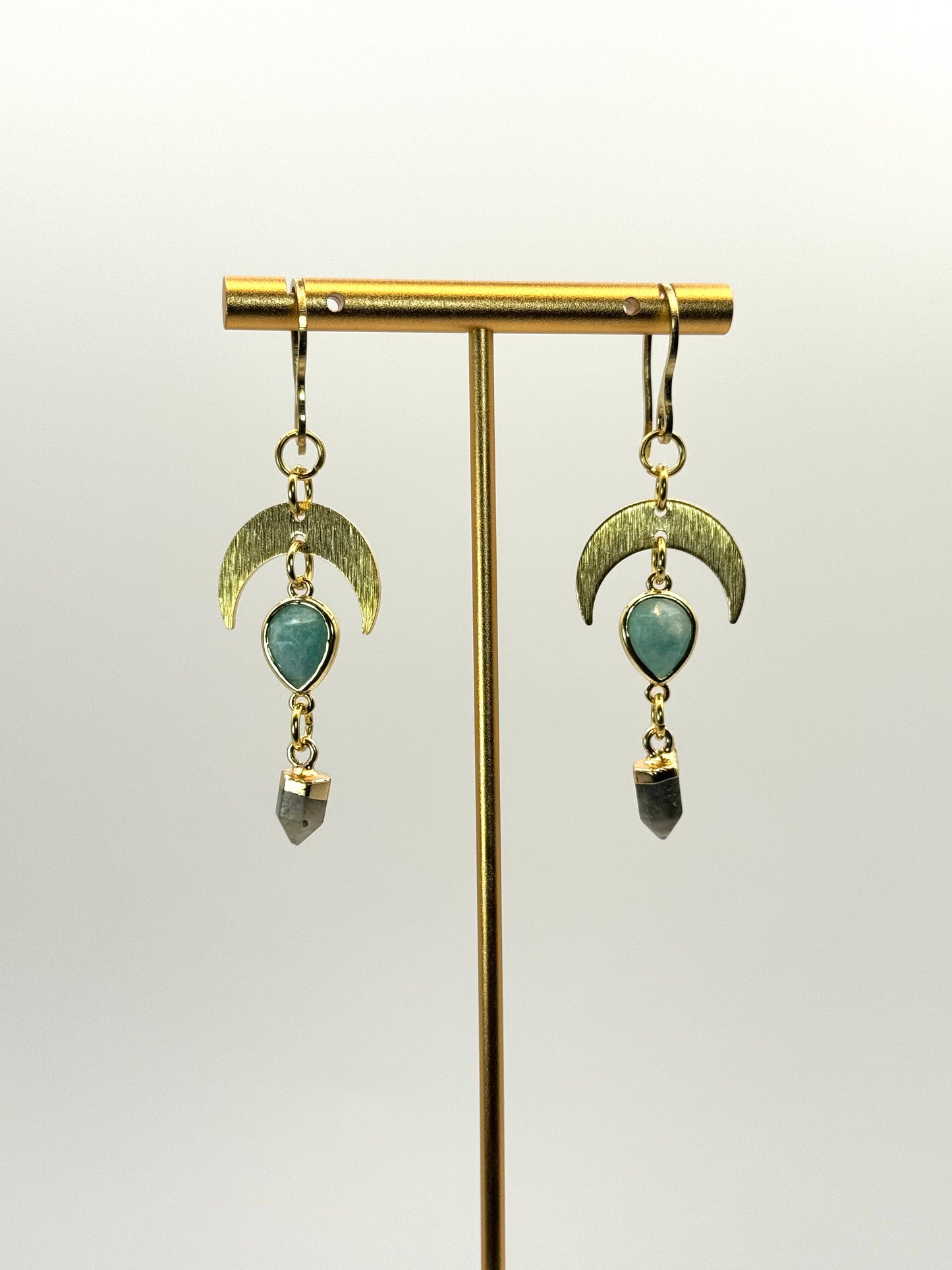 Pair of earrings with green gemstones on a gold stand against a white background