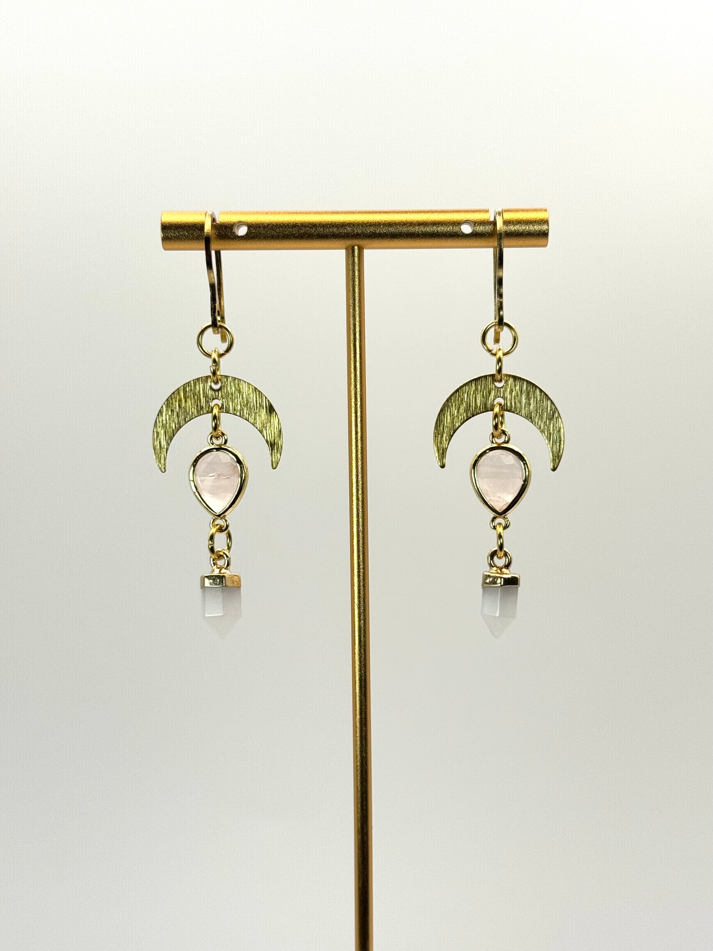 Gold earrings with moon phases and clear stones on a gold stand against a white background