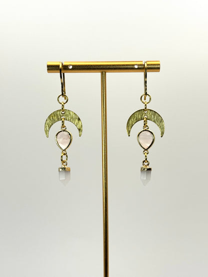 Gold earrings with moon phases and clear stones on a gold stand against a white background