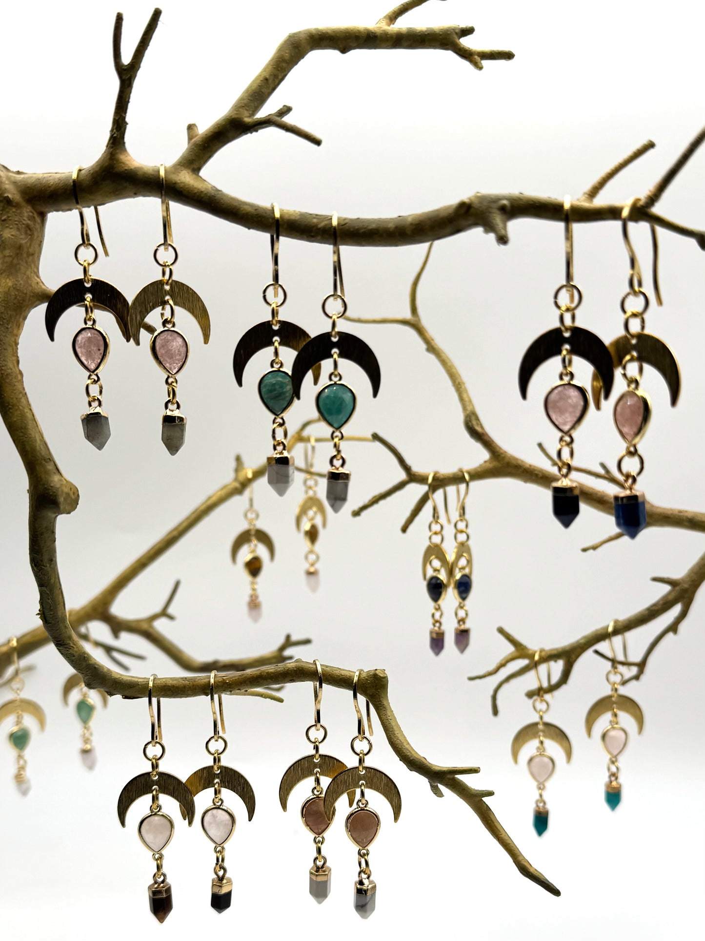 Collection of earrings hanging from a branch against a white background