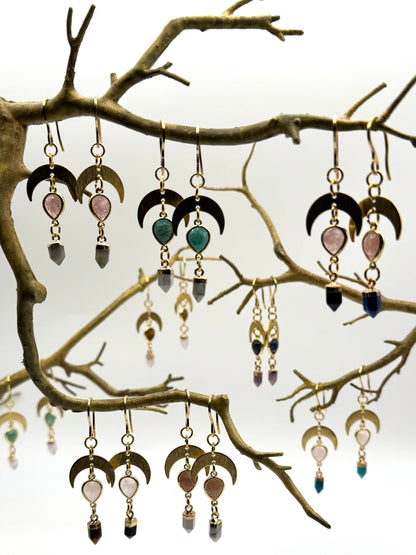 Collection of earrings hanging from a branch against a white background