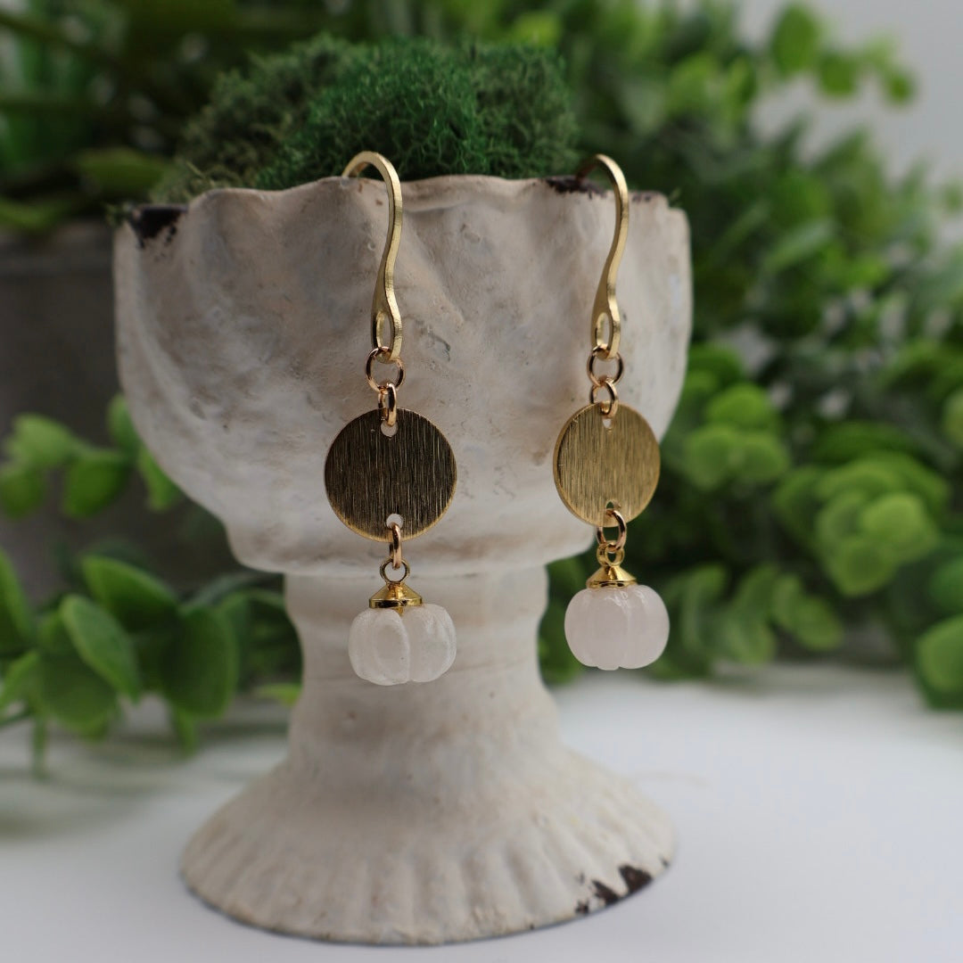 Pair of gold and rose quartz earrings on a shell stand with greenery in the background