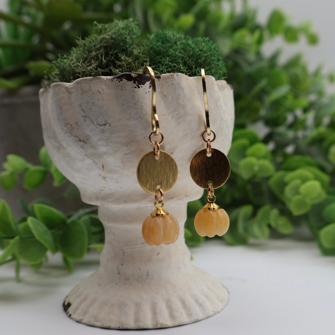 Gold and amber beaded earrings on a decorative stand with greenery in the background