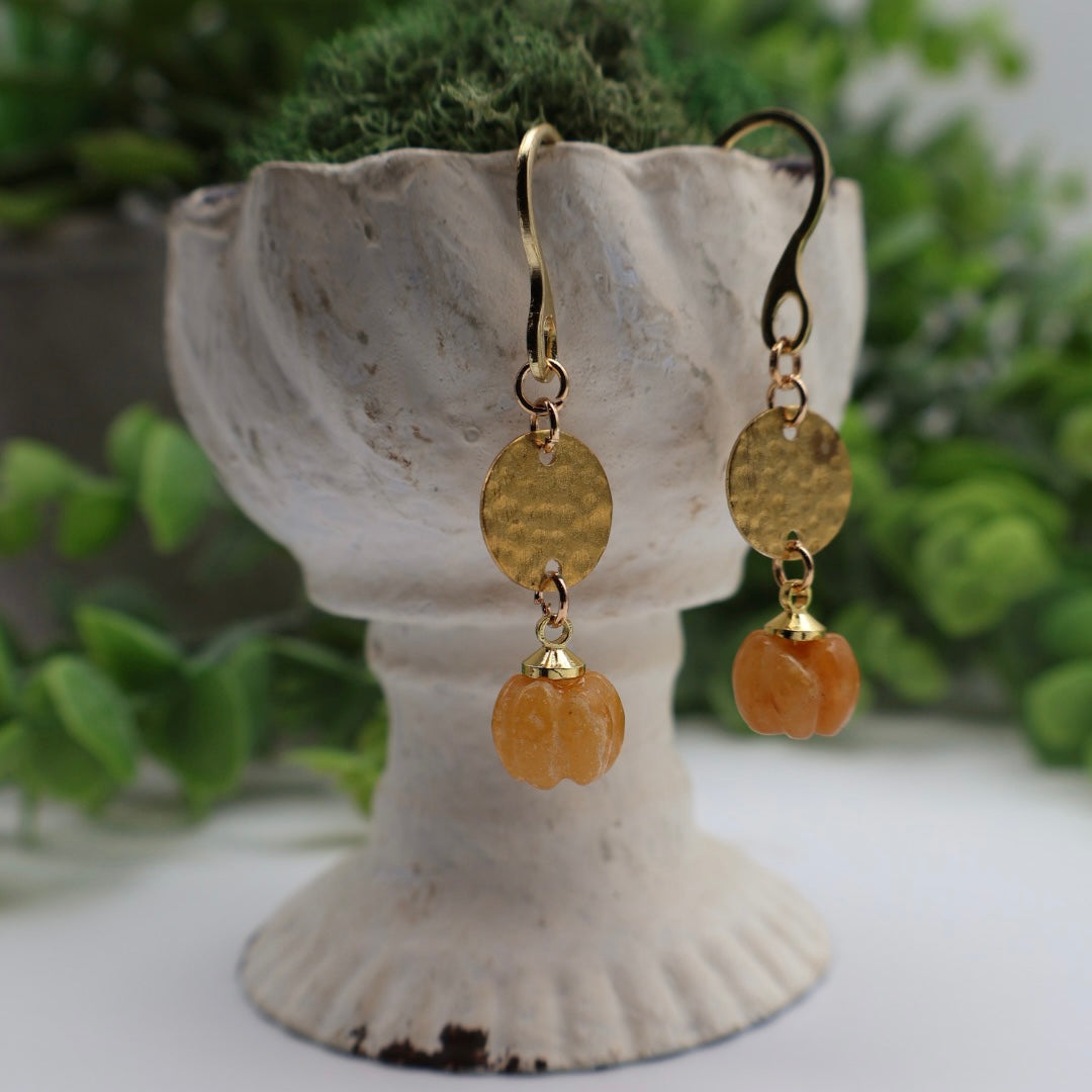 Gold and orange earrings on a decorative stand with a blurred green background