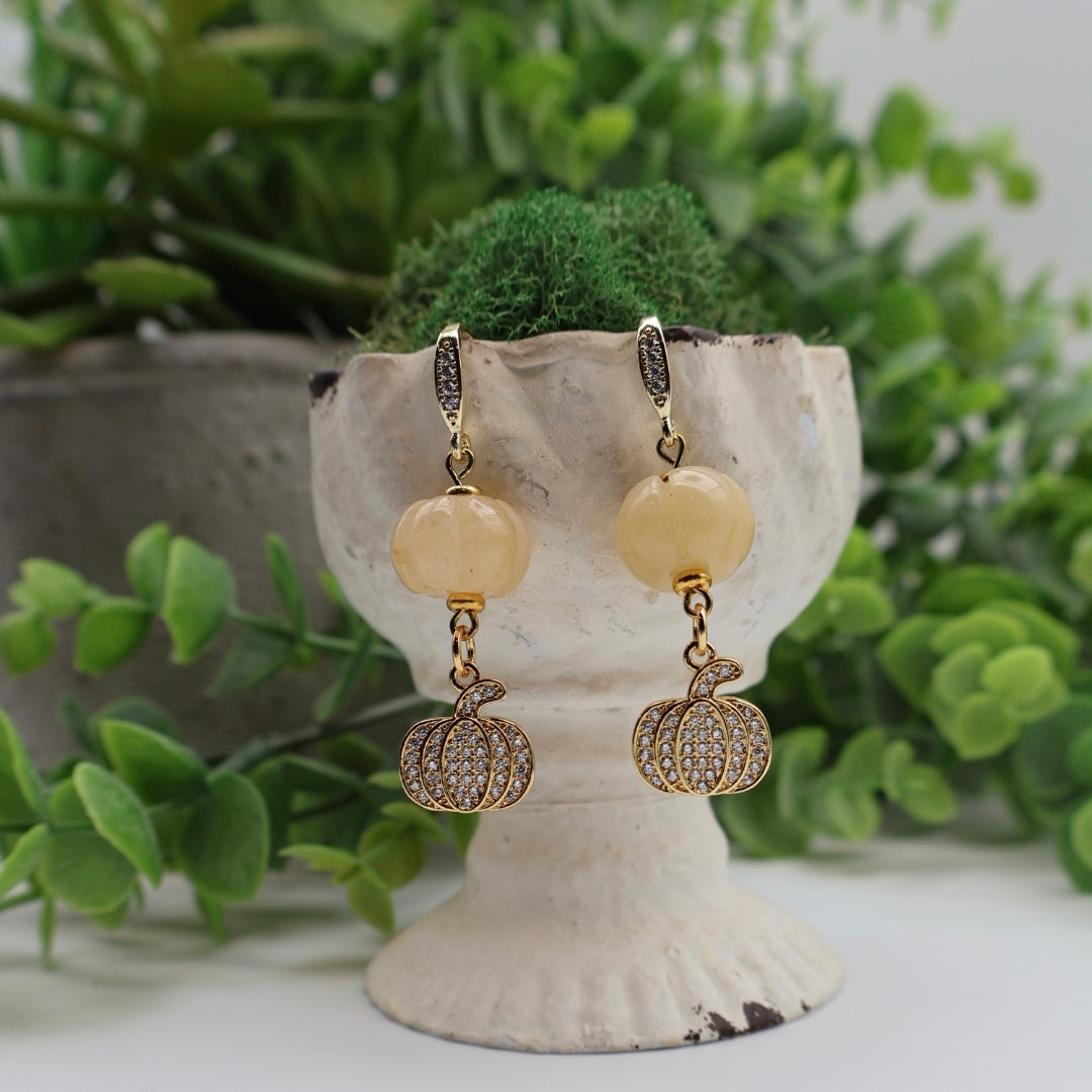 Pair of earrings with pumpkin and bead design on a decorative stand with plants in the background